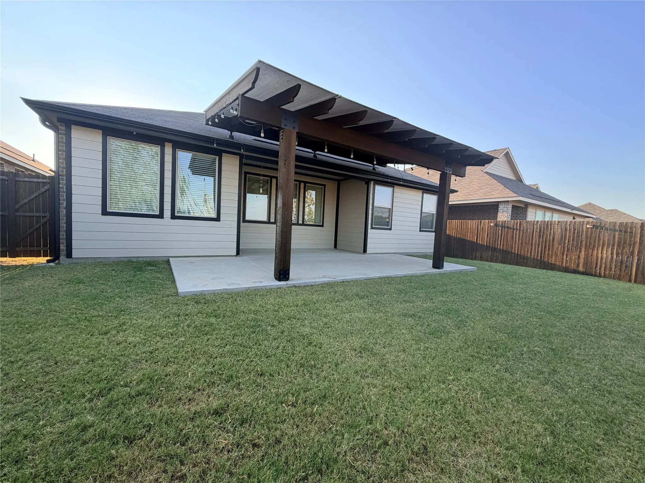 Expansive backyard featuring a concrete patio, wood-frame covered pergola, and privacy fencing