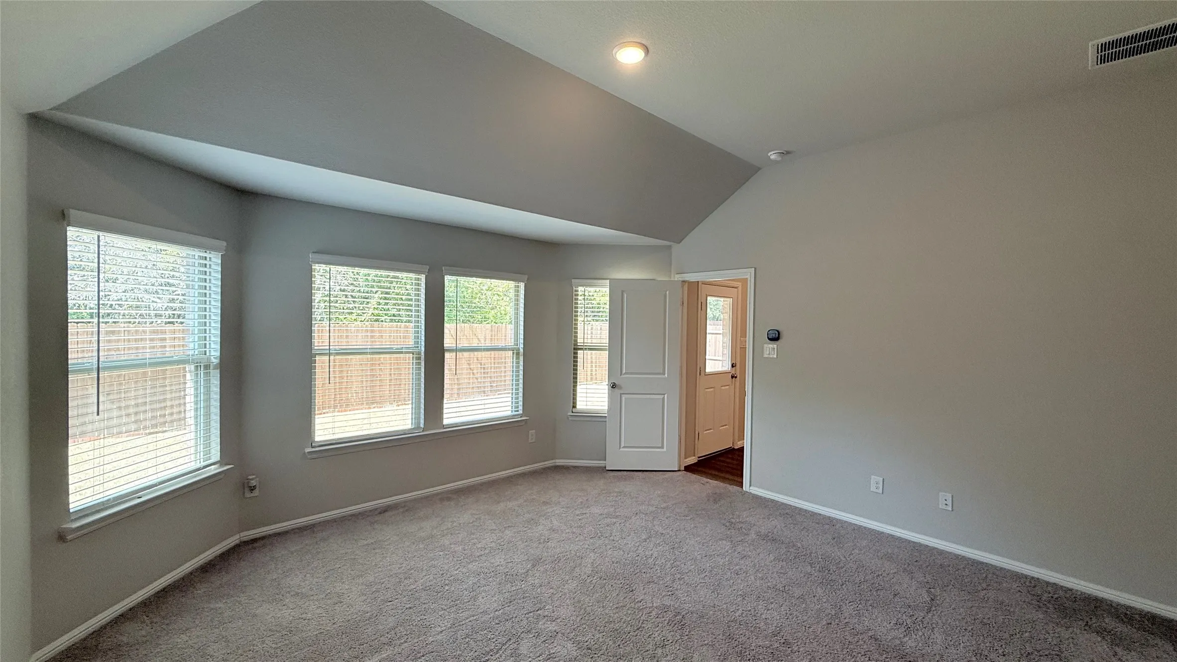 Vaulted ceiling, recessed lighting, multiple windows with blinds, neutral wall paint, and gray carpet flooring