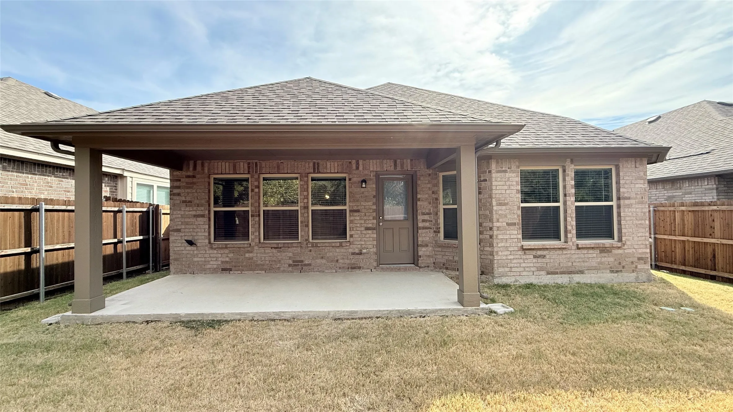 Covered patio with a concrete slab, brick exterior, and wooden fencing