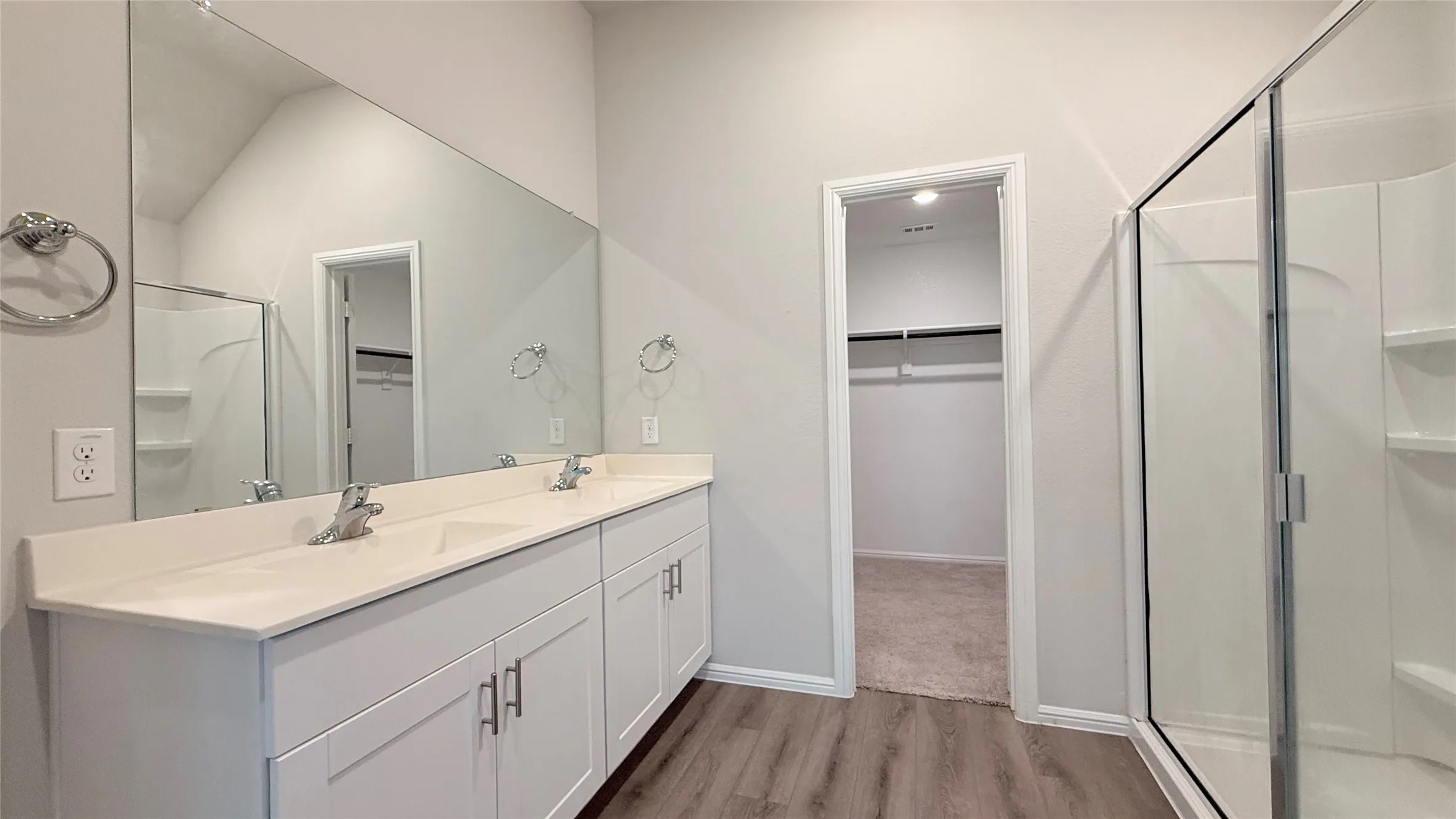 Dual vanity with undermount sinks, wood-finish flooring, full-width mirror, glass-enclosed shower, and built-in shower shelving