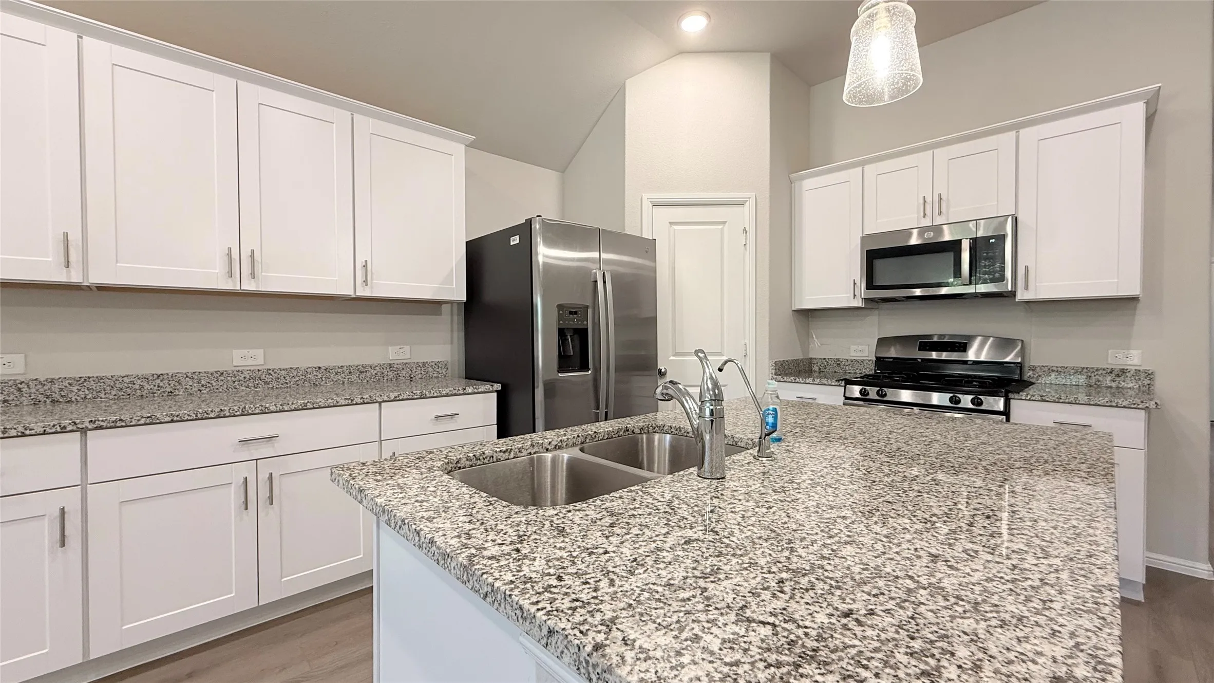 Kitchen featuring white shaker cabinetry, stainless steel appliances, granite countertops, and a center island with a double basin sink