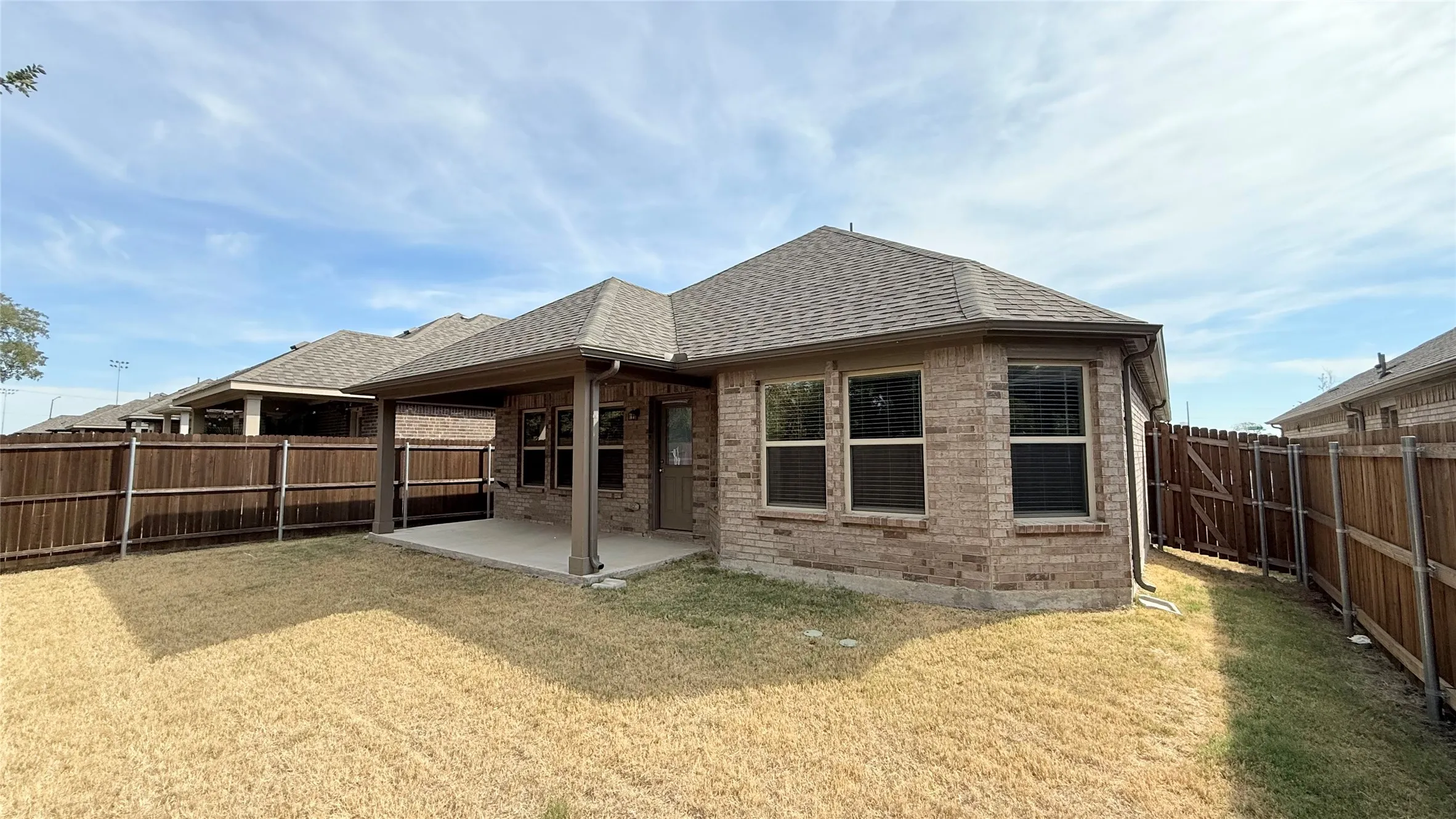 Brick exterior with a covered patio, shingled roof, and fenced yard