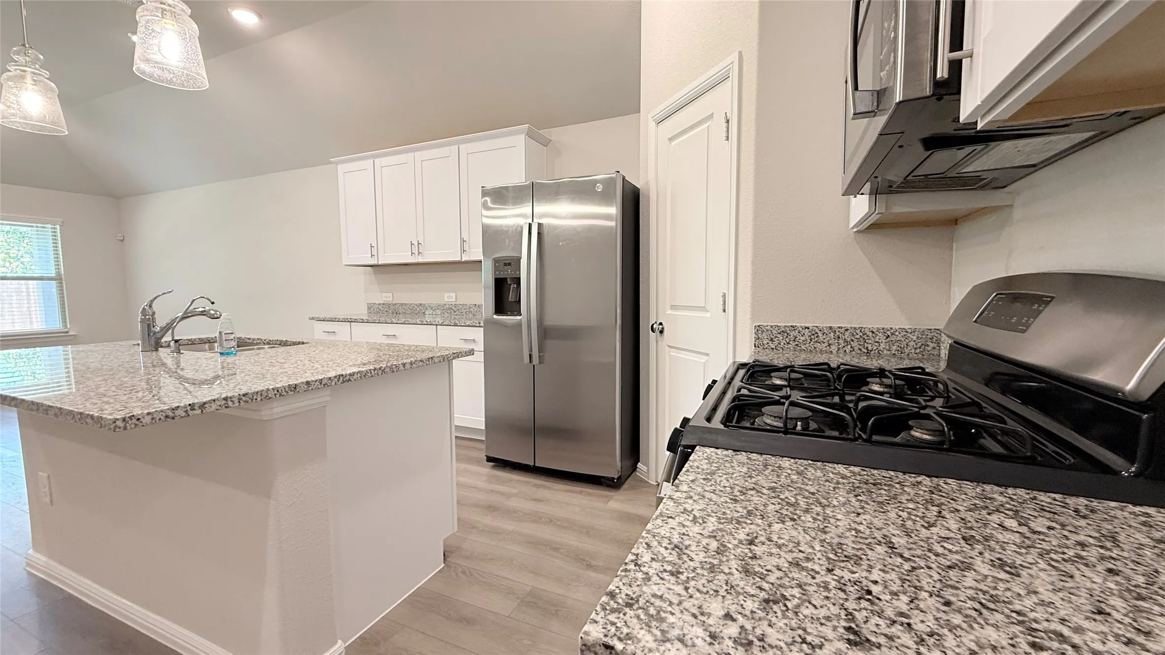 Kitchen featuring granite countertops, a gas range, white cabinetry, stainless steel appliances, and wood-finish flooring