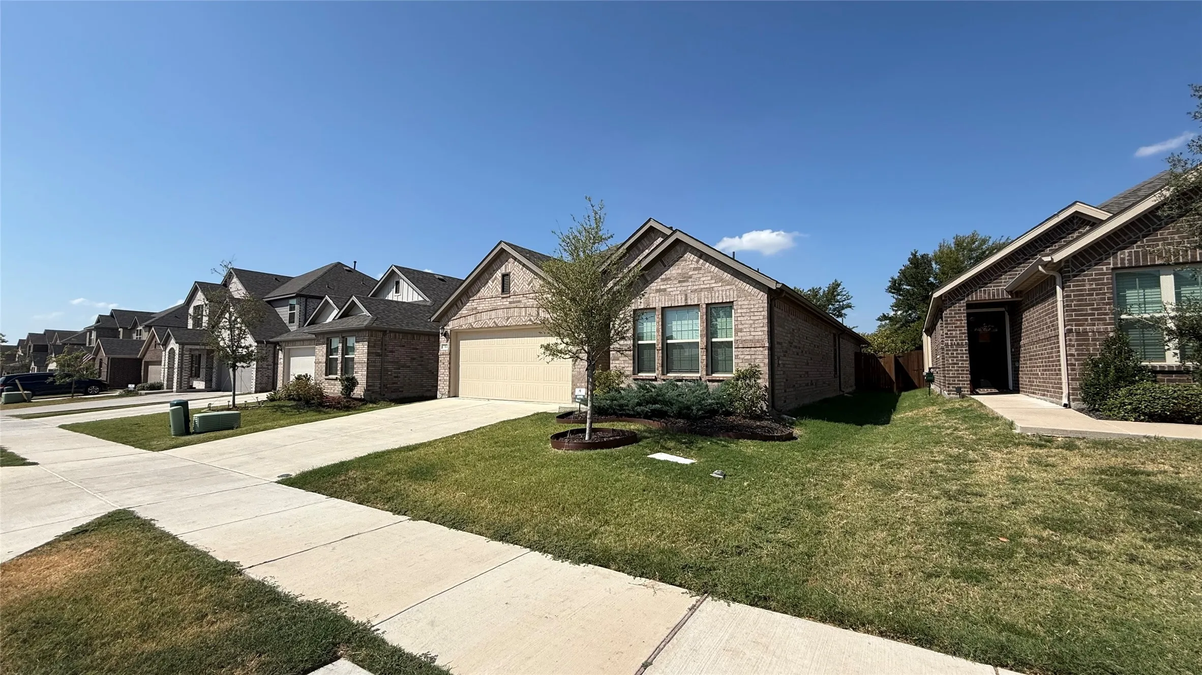 Brick exterior, attached garage, concrete driveway, front landscaping, and a manicured lawn