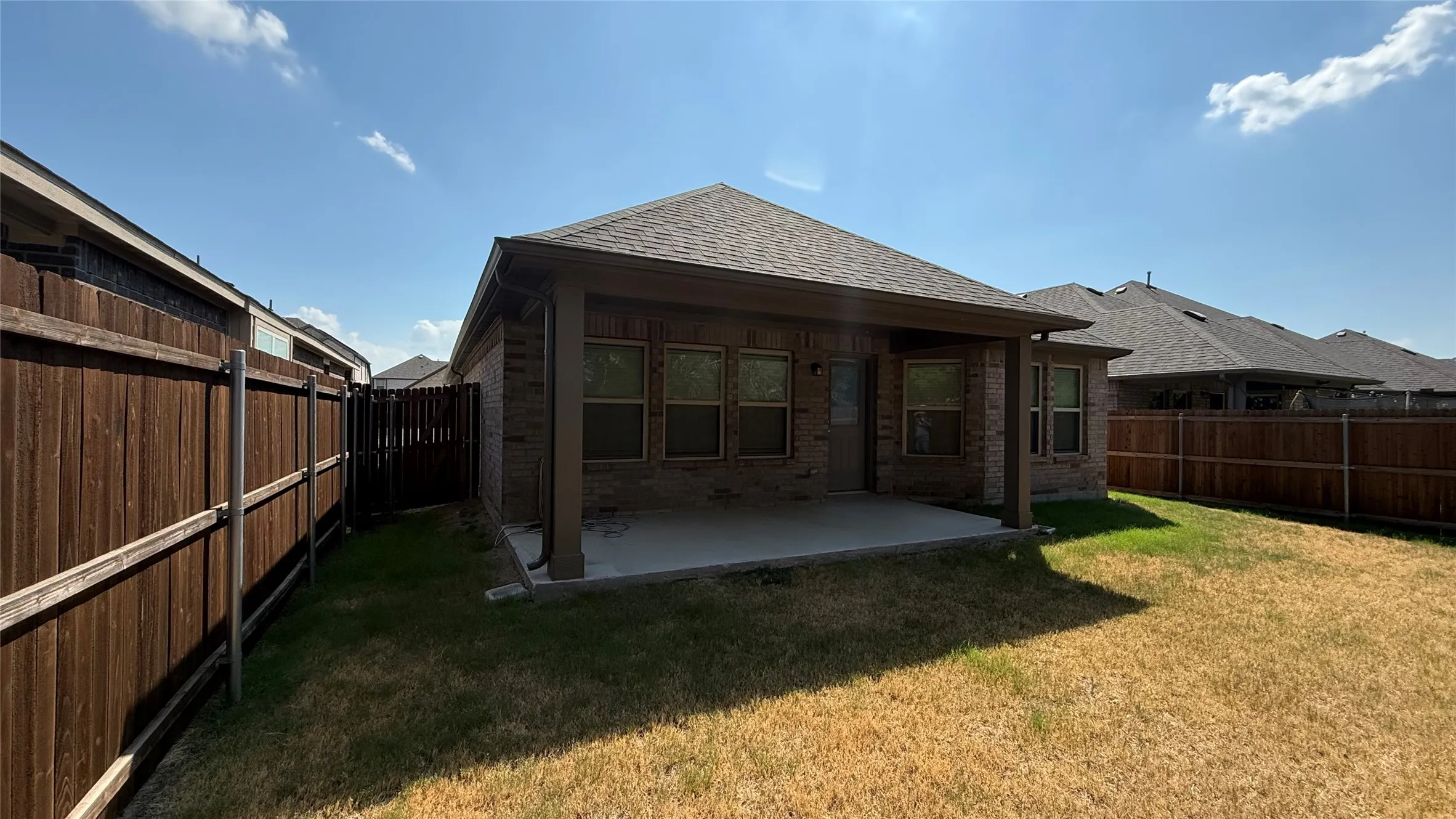 Brick exterior featuring a covered patio, concrete slab, and wood privacy fence