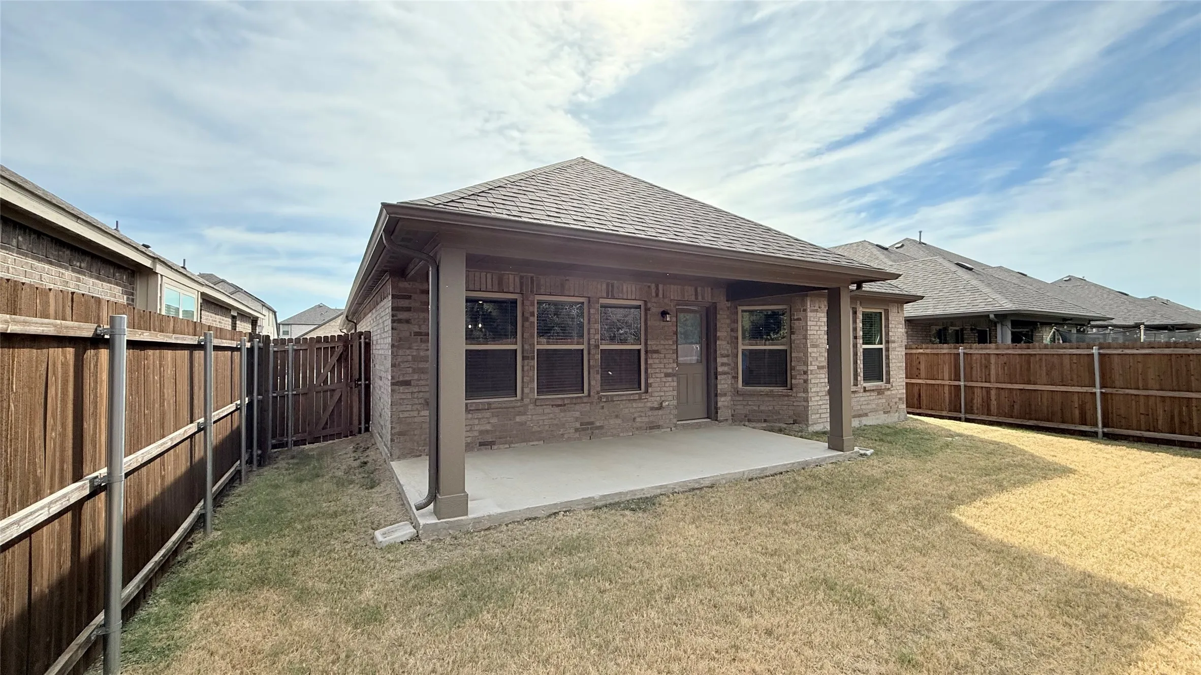 Covered patio with a concrete slab, brick exterior, and wooden fencing