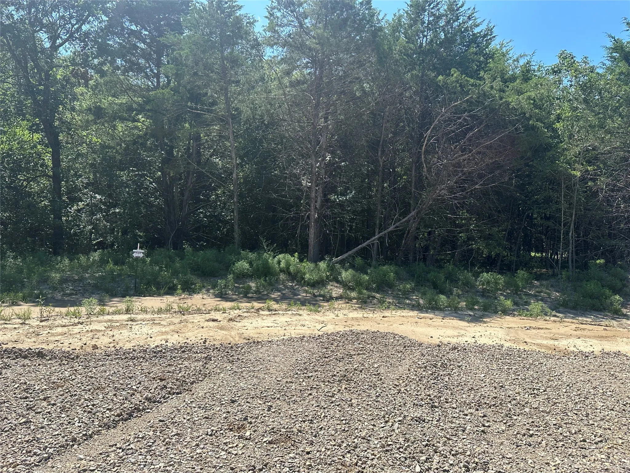 Cleared lot featuring a natural tree line and gravel base