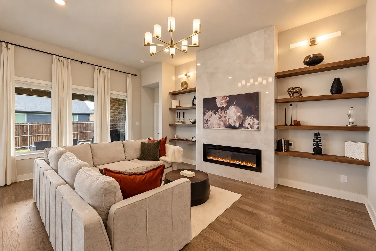 Spacious great room designed for both entertaining and everyday living, featuring custom lighting, built-in wood shelving, and a striking floor-to-ceiling porcelain-tiled electric fireplace with adjustable ambiance and heat. A built-in media box allows for a clean, flush-mounted TV with no exposed wires.