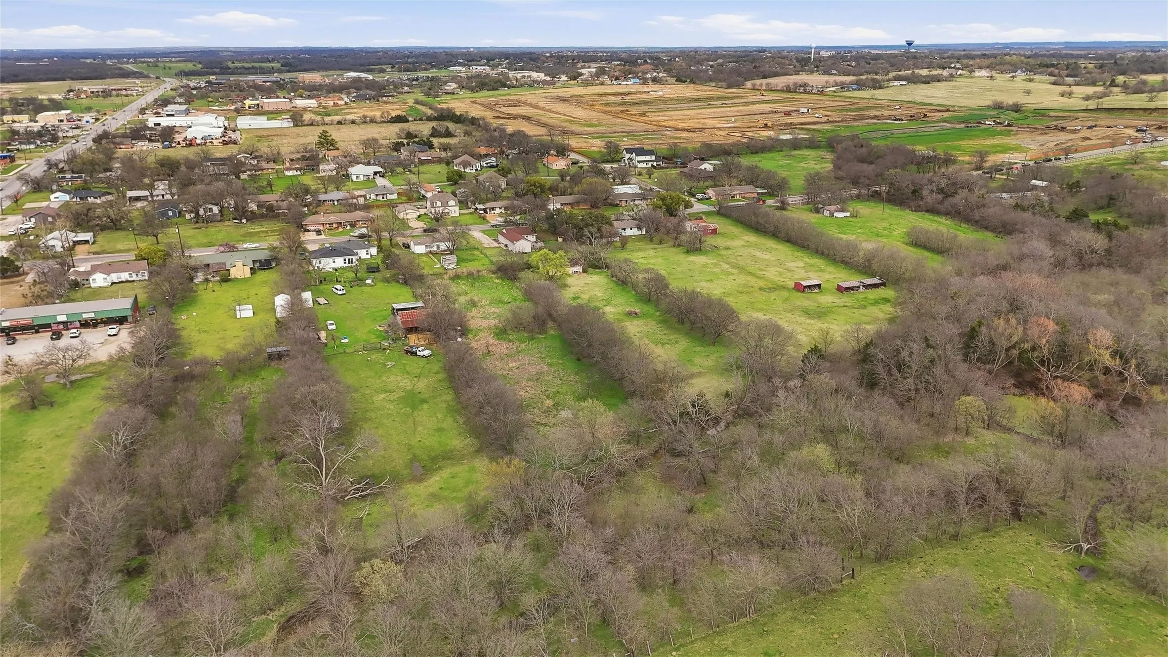 Expansive land with a mix of wooded and grassy areas, featuring multiple outbuildings and residential structures