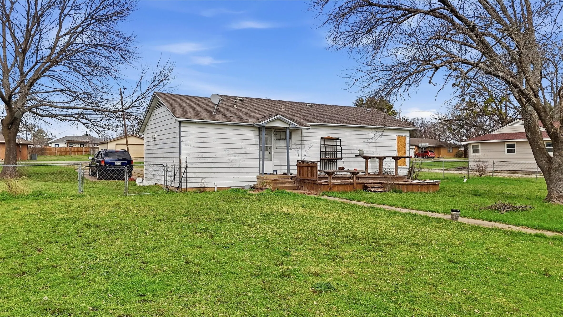 Rear exterior featuring a wood deck, white siding, and a brown shingle roof