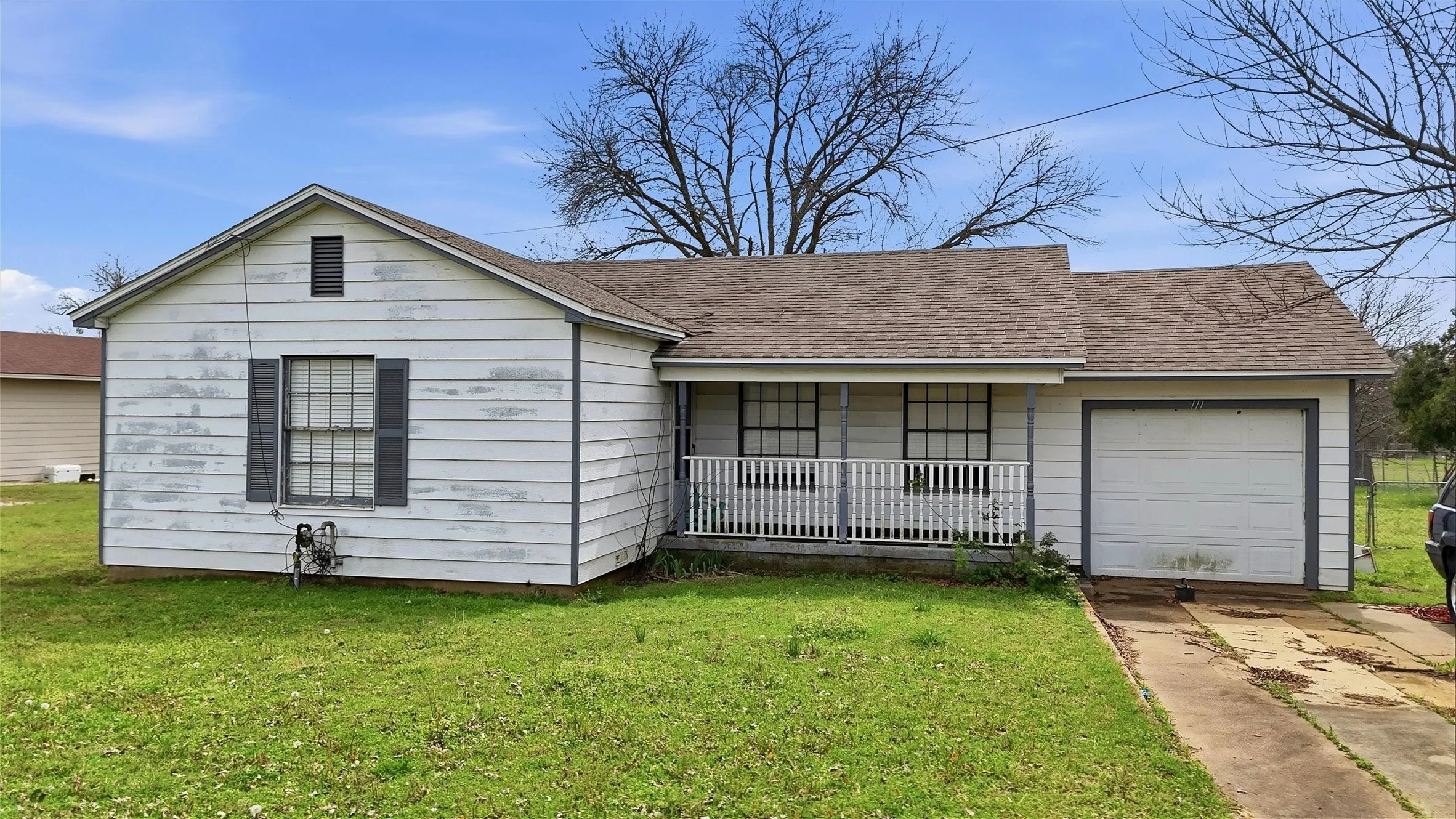 White siding exterior with a partial covered porch, attached garage, and a gable roofline