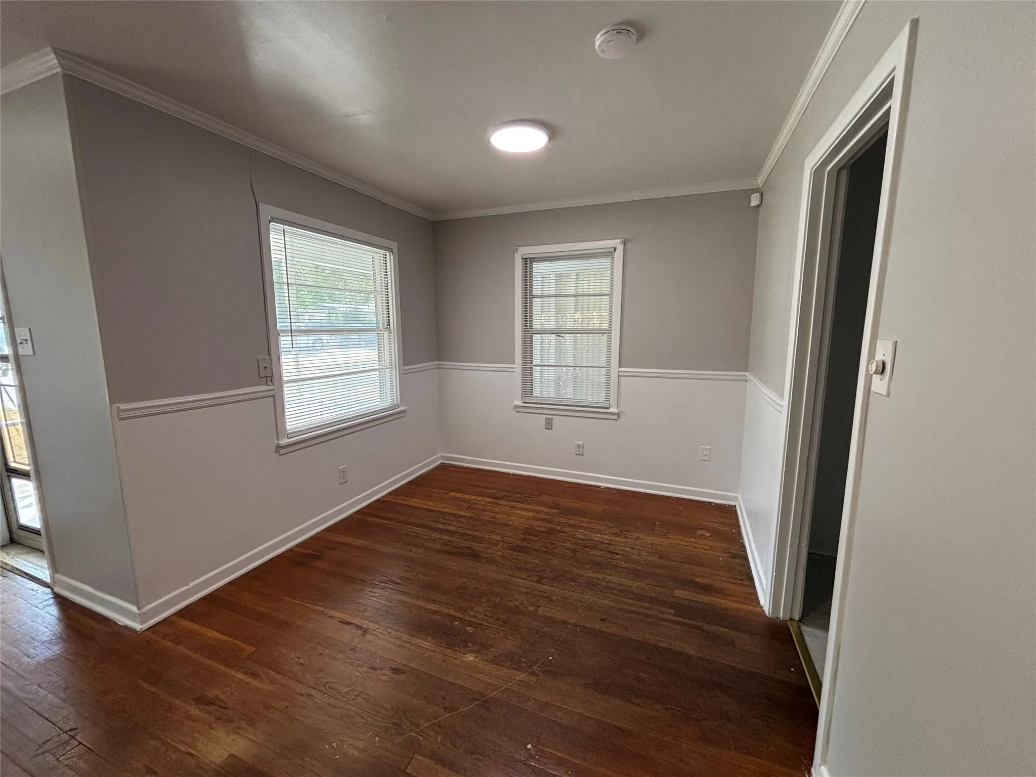 Hardwood flooring, painted walls with wainscoting, two windows, crown molding, and recessed lighting fixture