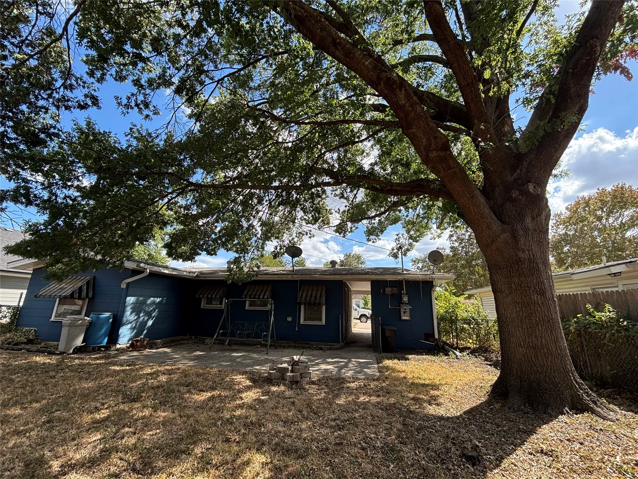 Expansive backyard featuring a large mature tree, partial hardscaping, and blue exterior siding