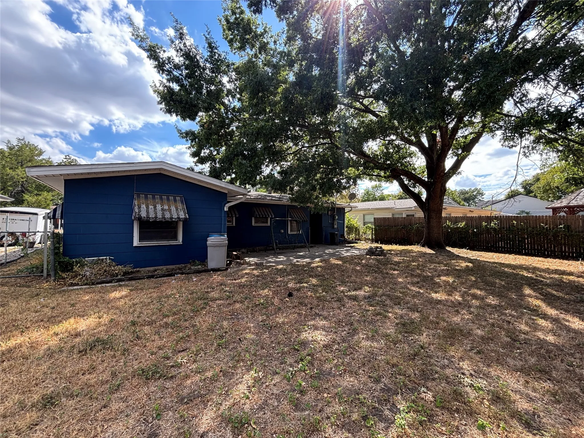 Expansive backyard featuring a mature tree, wooden privacy fence, and a patio area