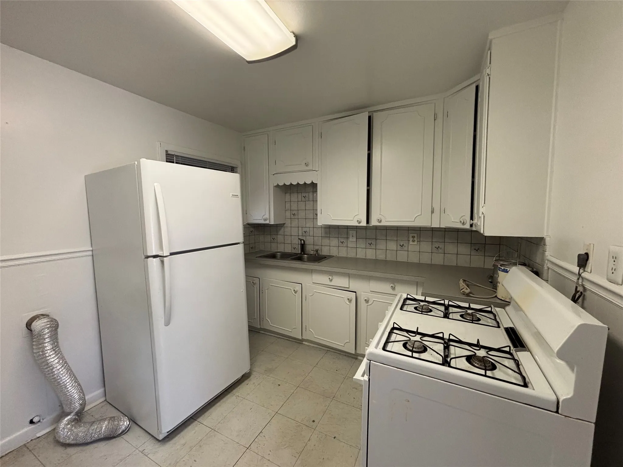 Kitchen space featuring white cabinetry, a double-basin sink, tile backsplash, and a gas range