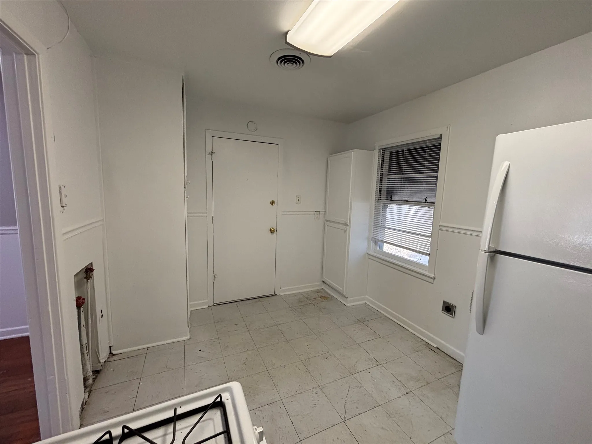 White tile flooring, built-in storage cabinet, window with blinds, paneling detail, white refrigerator