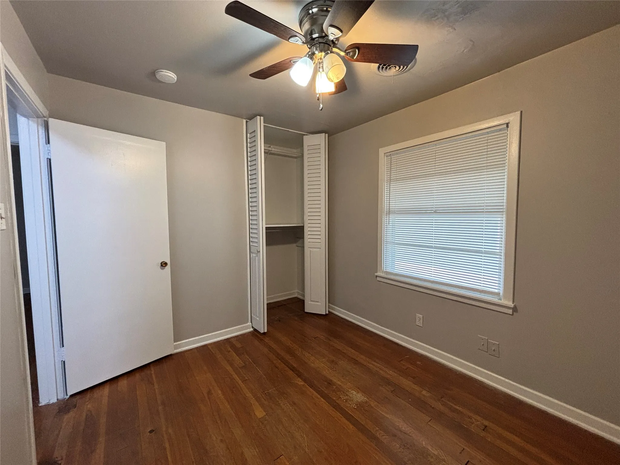 Wood-finish flooring, ceiling fan with integrated lighting, window with blinds, and bi-fold closet doors