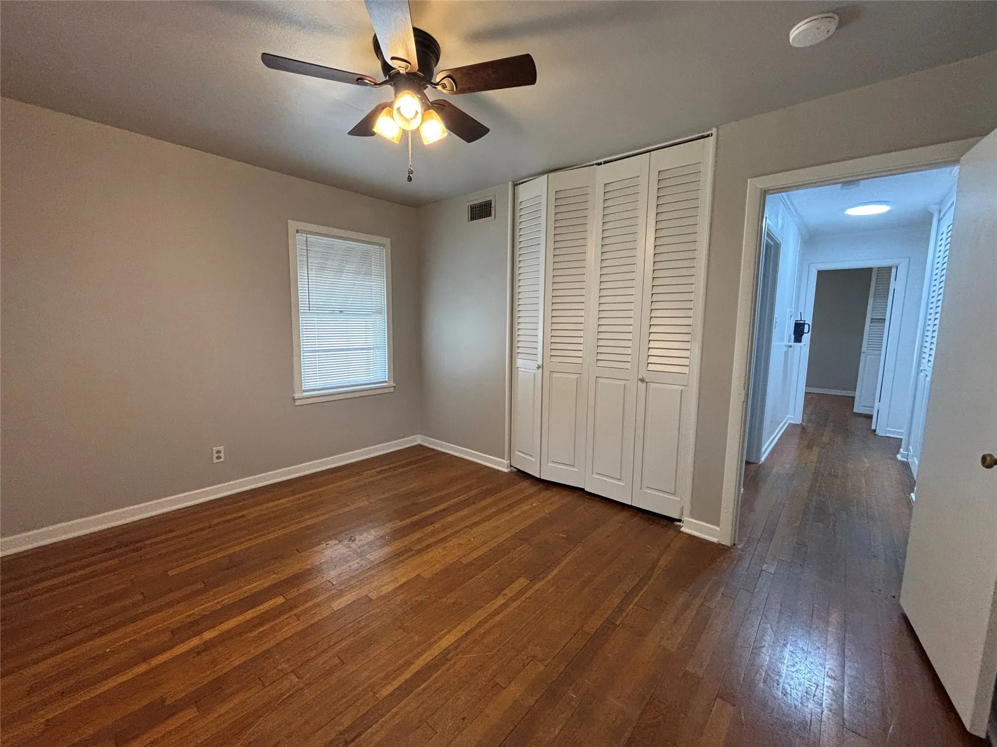 Hardwood flooring, ceiling fan with integrated lighting, louvered bi-fold closet doors, and recessed window