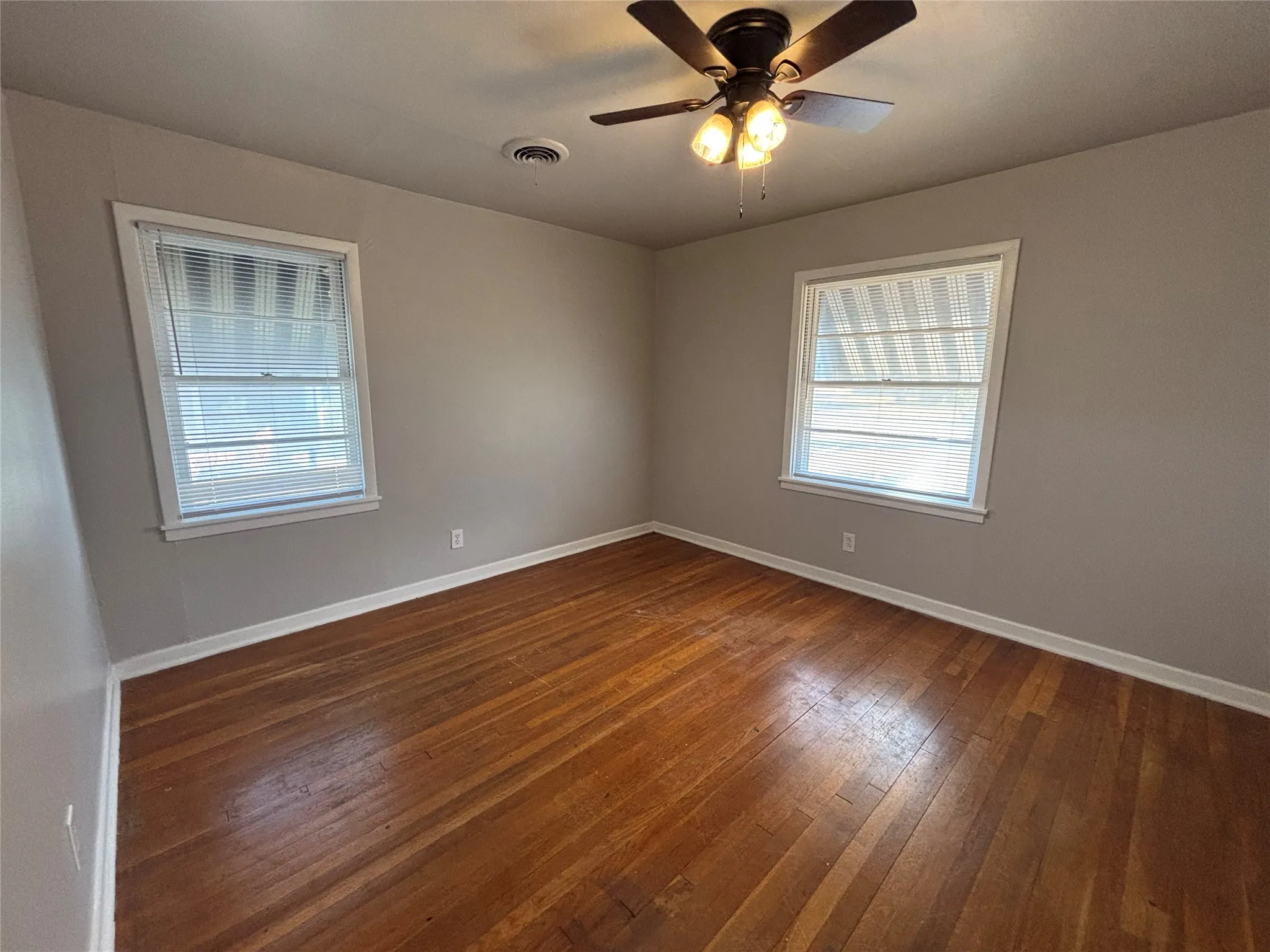 Hardwood flooring, painted walls, two windows with blinds, and a ceiling fan with integrated lighting