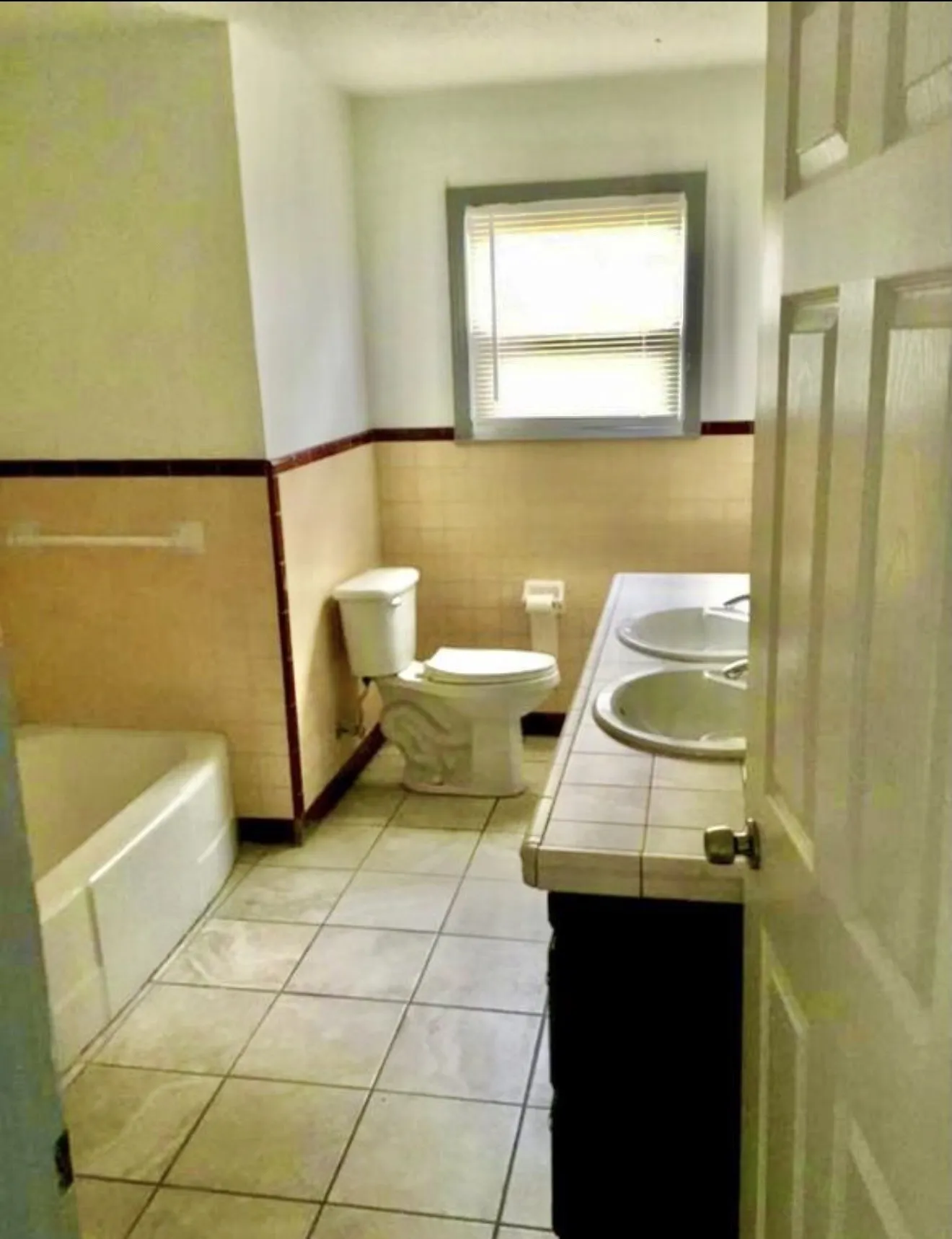 Ceramic tile flooring, dual vanity with tile countertop, window with blinds, toilet and bathtub