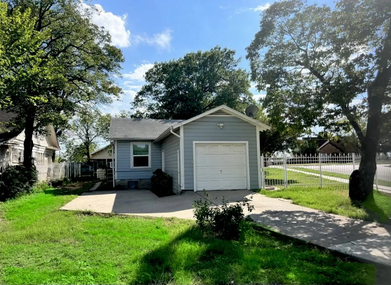 Attached single-car garage, concrete driveway and a white metal fence.