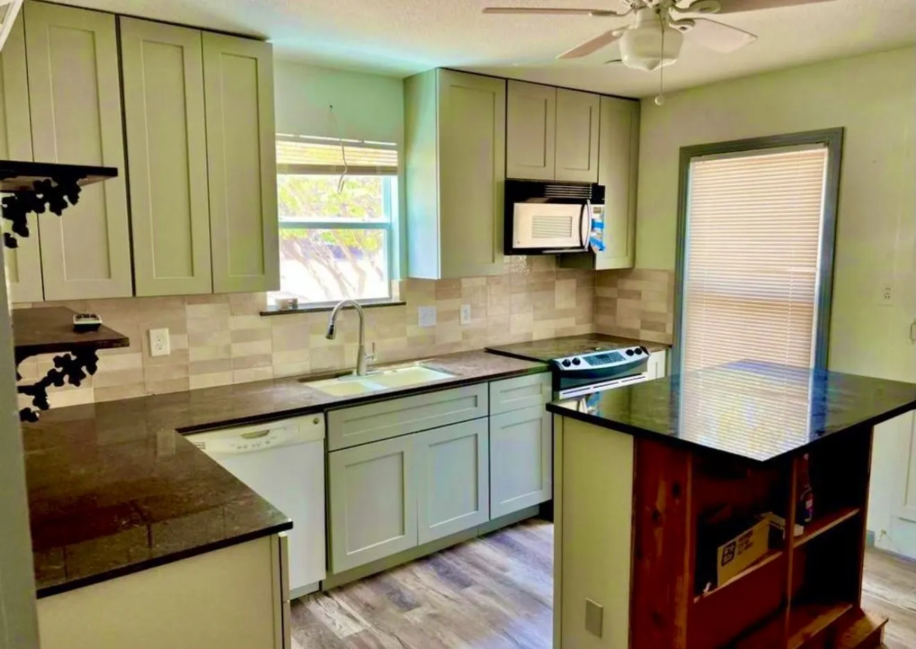 Full kitchen with light-toned cabinetry, range oven, dishwasher, microwave and built in spice rack.