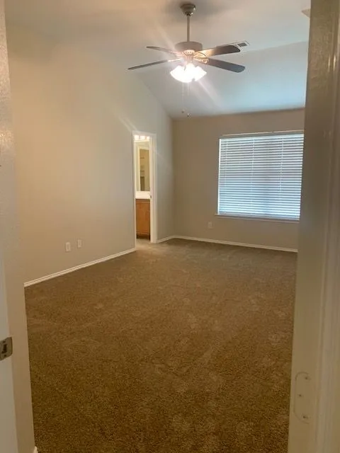 Spacious room featuring vaulted ceilings, ceiling fan with light kit, wall-to-wall carpeting, and a window with horizontal blinds