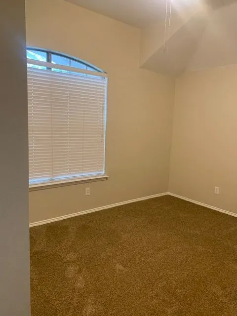 Arched window with blinds, vaulted ceiling, and neutral carpet flooring