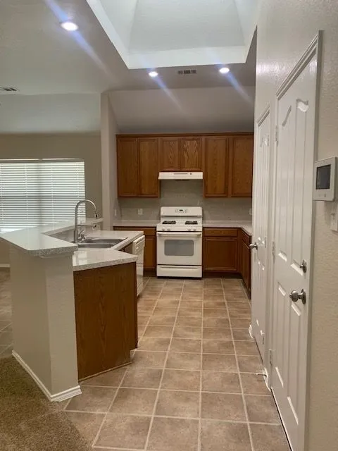 Kitchen featuring wood cabinetry, solid surface countertops, tile flooring, and white appliances