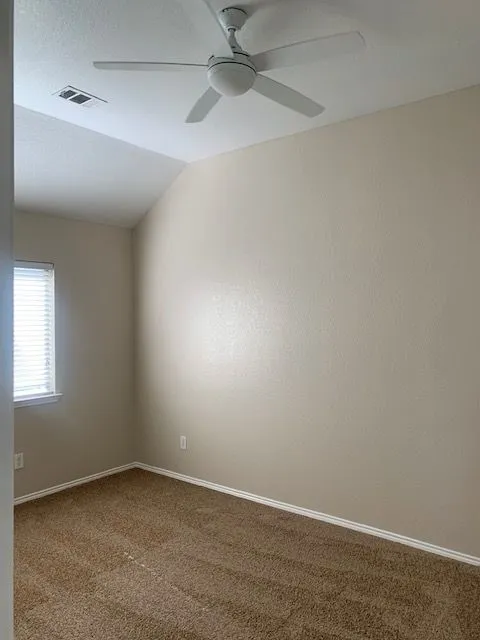 Sloped ceiling with an integrated ceiling fan, neutral wall paint, white trim, and brown carpeting