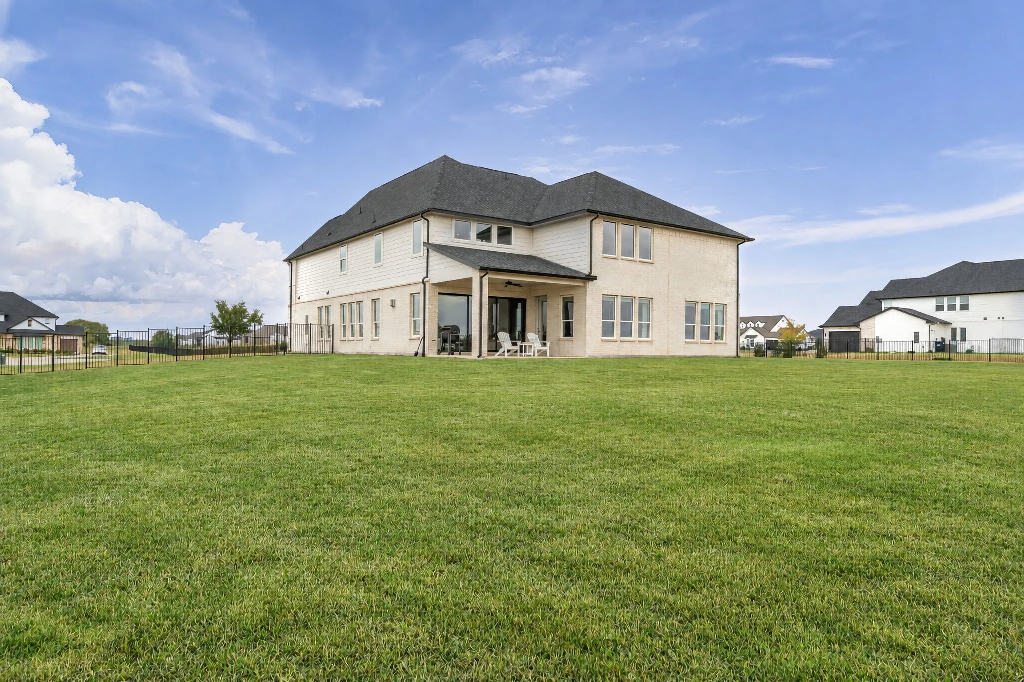 Expansive backyard with a manicured lawn, full height windows, and a covered patio