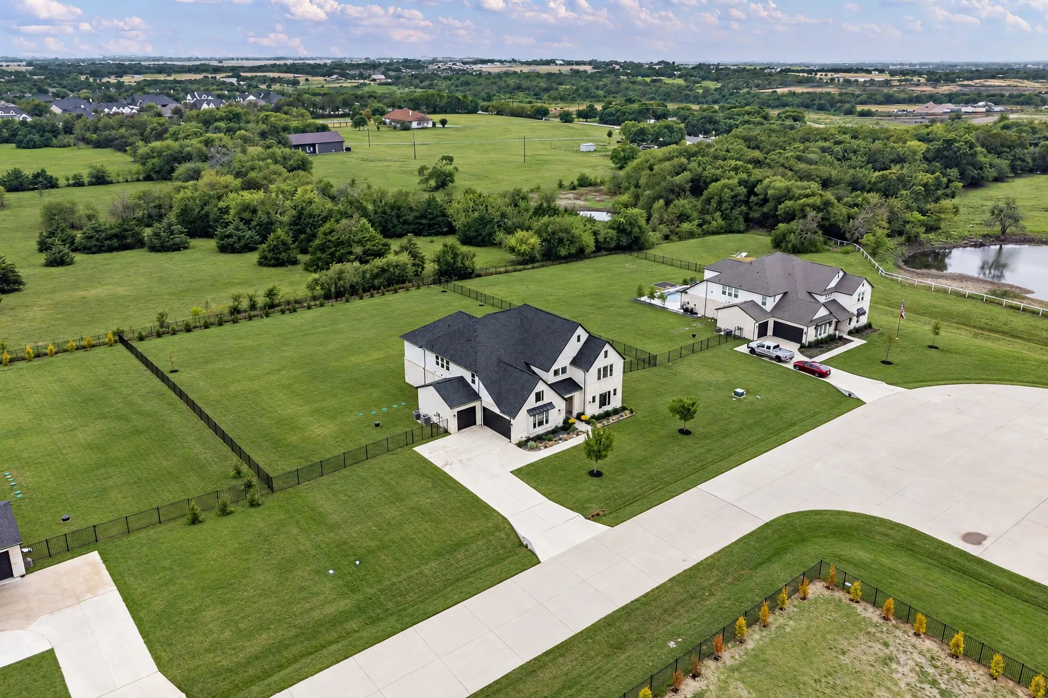 Expansive green spaces featuring a modern residence with a dark roof, private fencing, and a concrete driveway