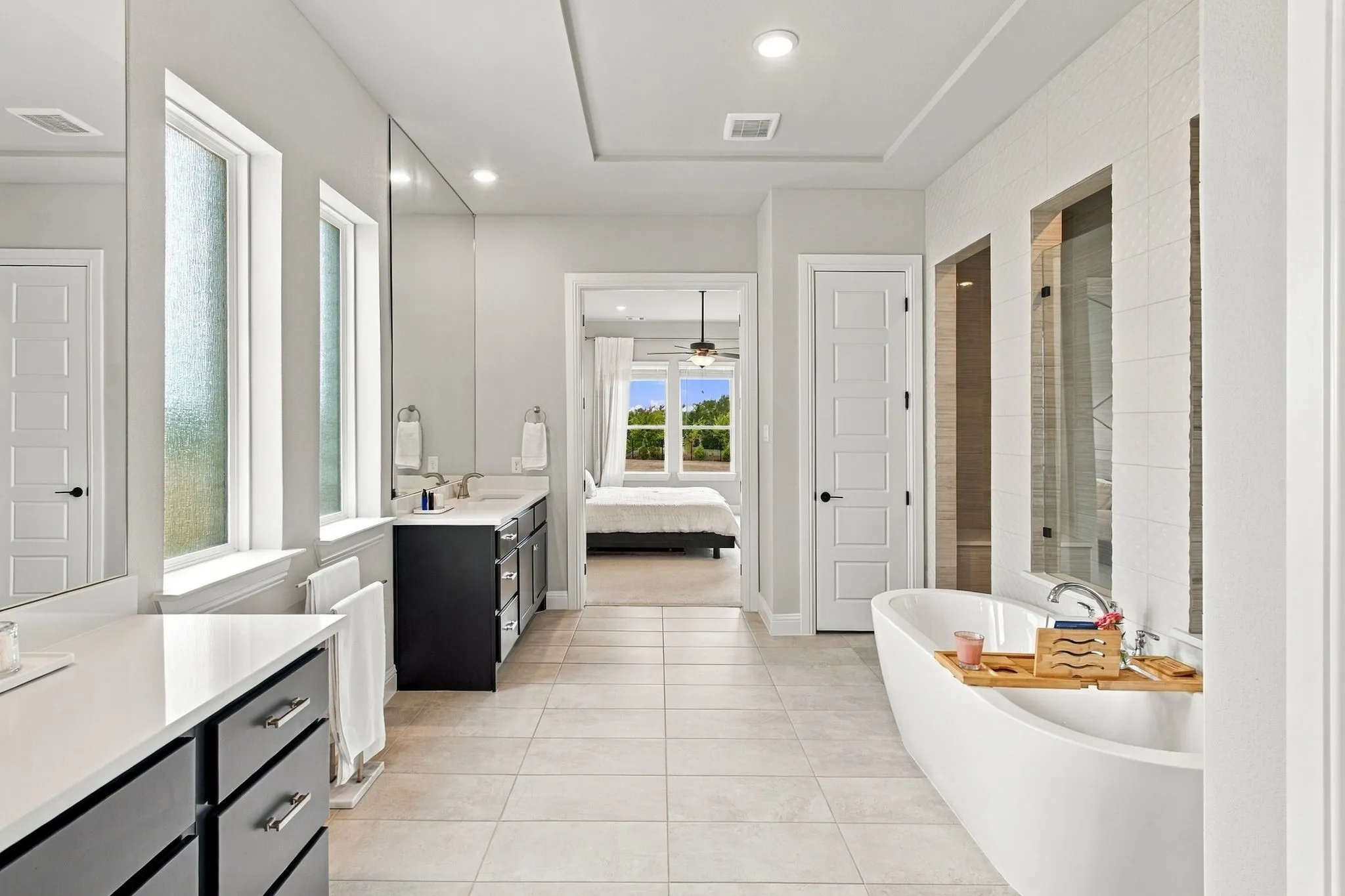Freestanding soaking tub, dual vanities with dark cabinetry, tile flooring, and a walk-in shower with glass enclosure
