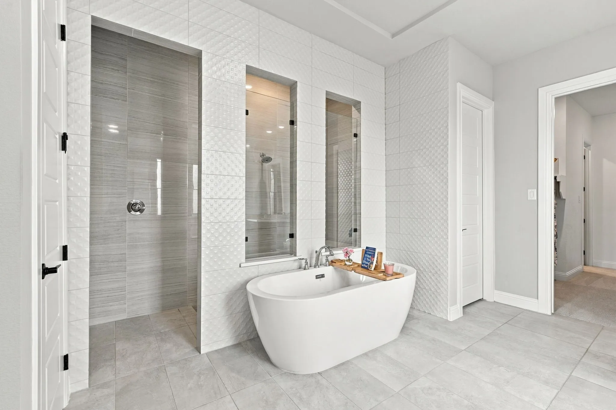 Freestanding soaking tub, walk-in shower with glass enclosure, large format tile flooring, and textured white wall tile