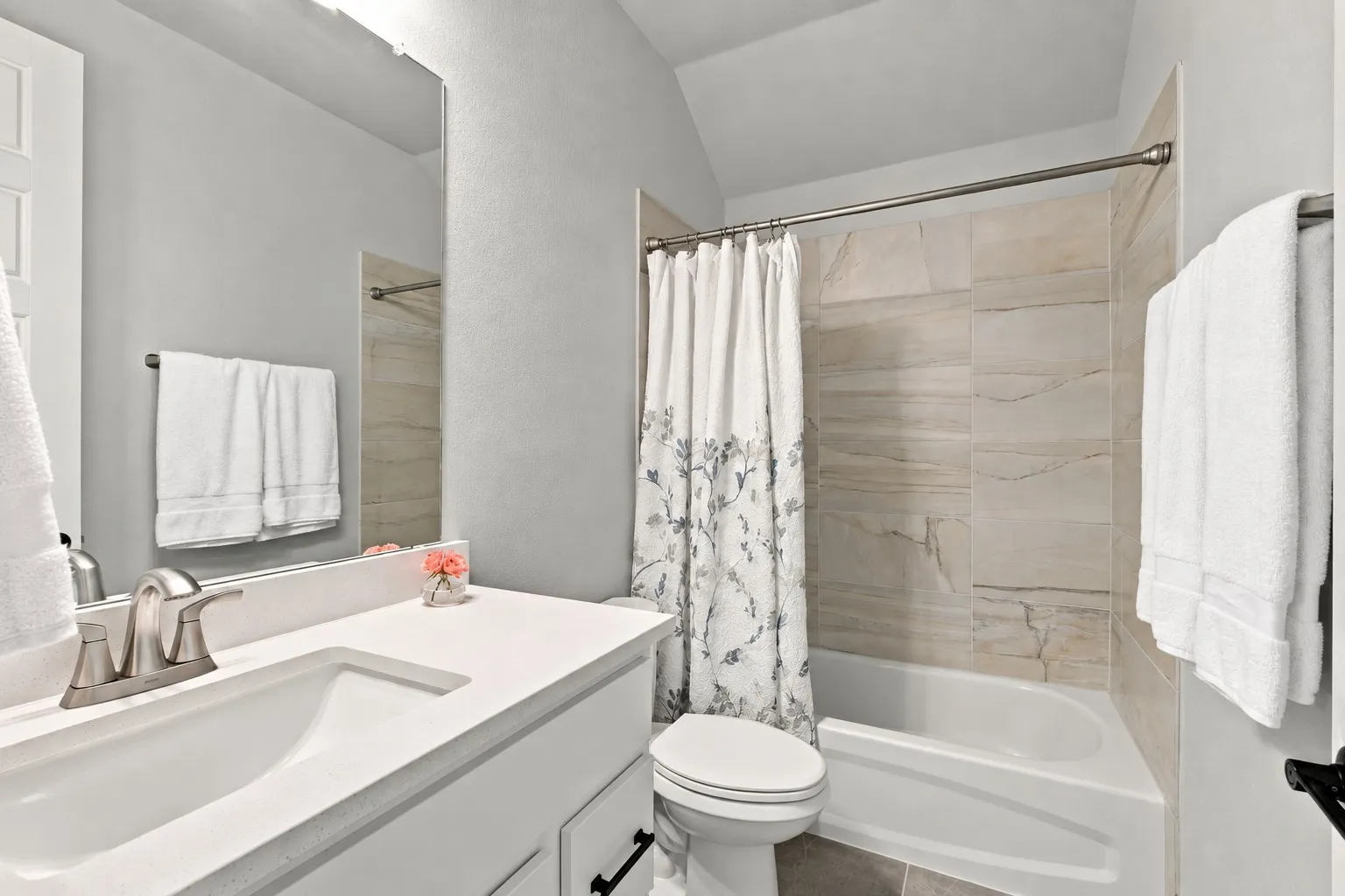 White vanity with integrated sink, brushed nickel faucet, tiled shower surround, and built-in bathtub