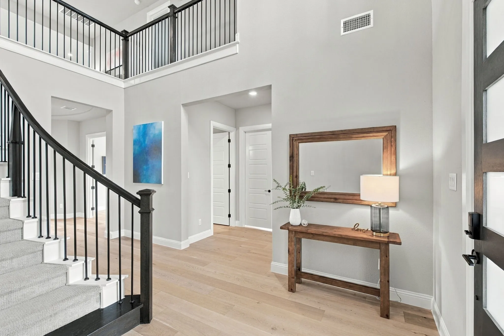 Two-story foyer with a curved staircase featuring black iron balusters, light wood-finish flooring, and a second-story landing with matching balusters