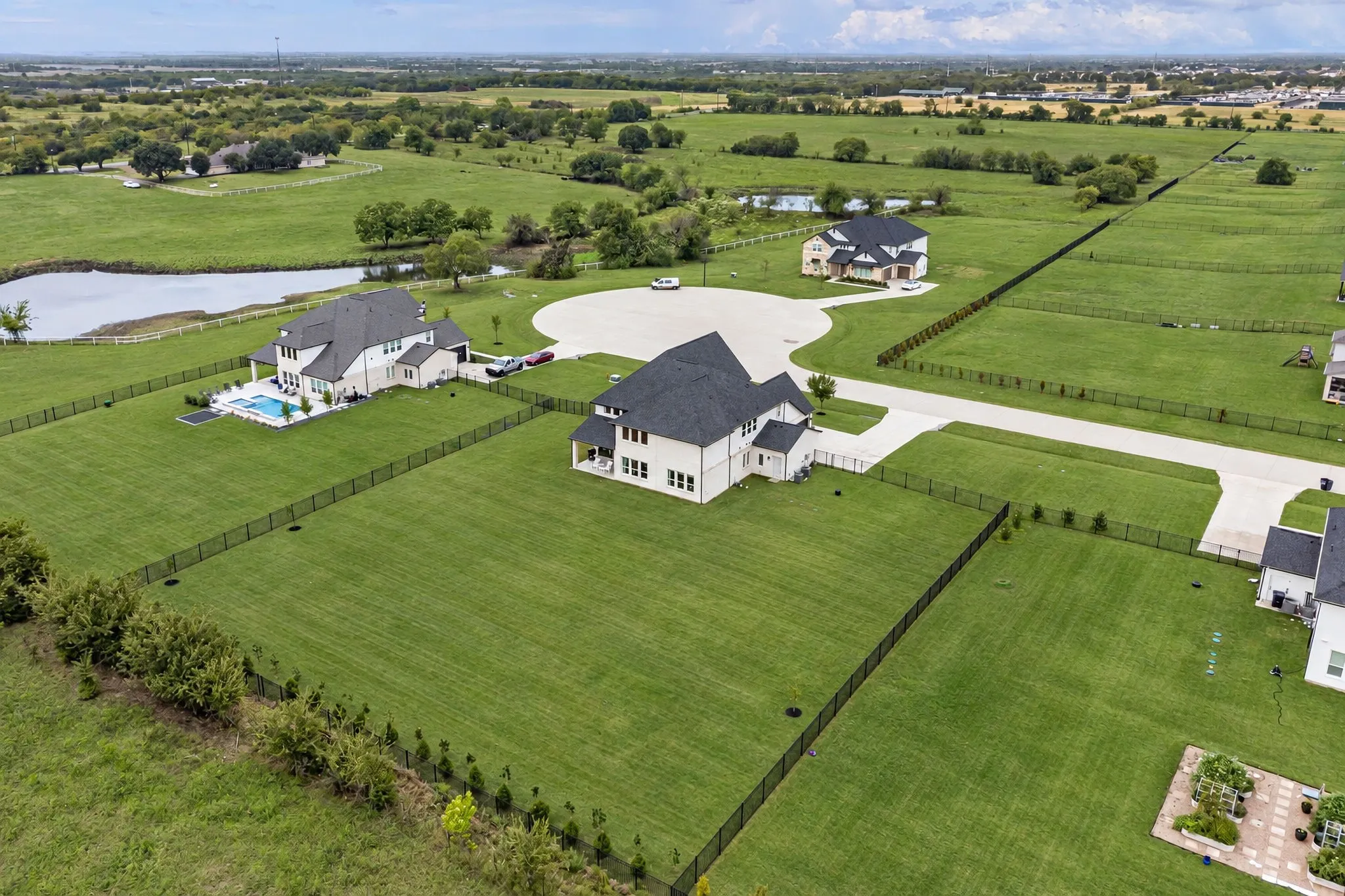 Residential property with expansive grassy lots, black metal fencing, and a private swimming pool
