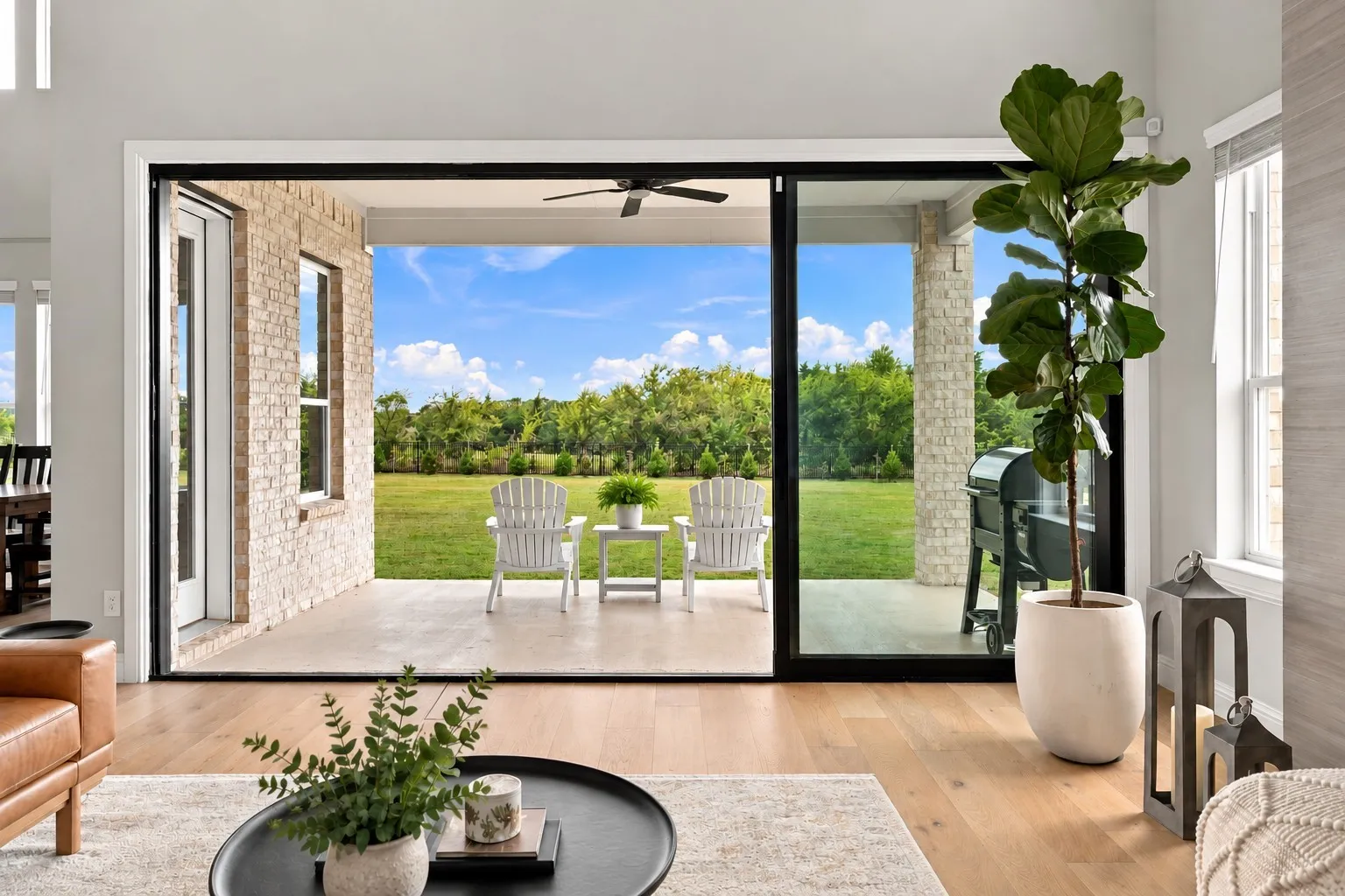 Expansive concrete patio with a ceiling fan, brick exterior wall, and stone column accents, featuring large sliding glass doors and wood-finish flooring