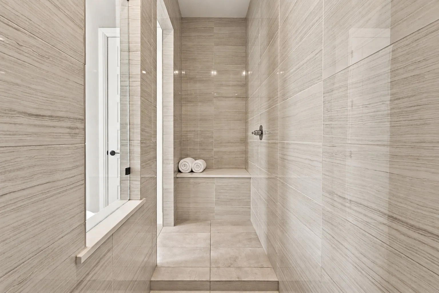Tiled walk-in shower featuring a built-in bench, integrated shower head, and light-toned horizontal tiling