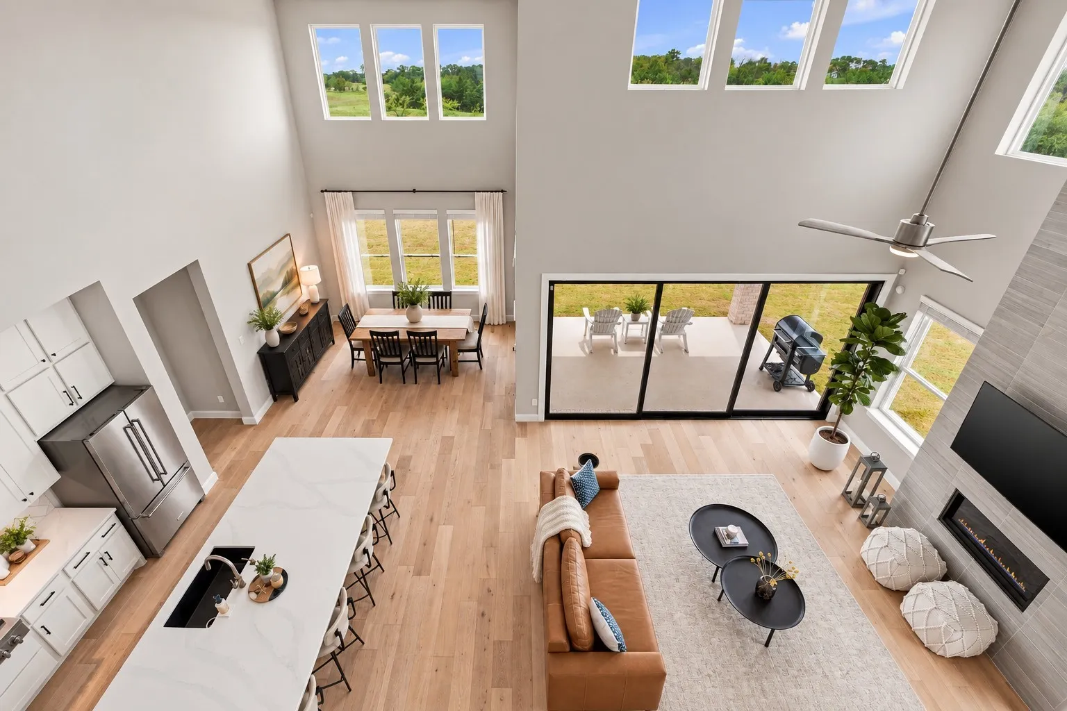 Soaring ceilings with transom windows, wood-finish flooring, a contemporary linear fireplace, an expansive kitchen island with a rectangular sink, and sliding glass doors to a patio