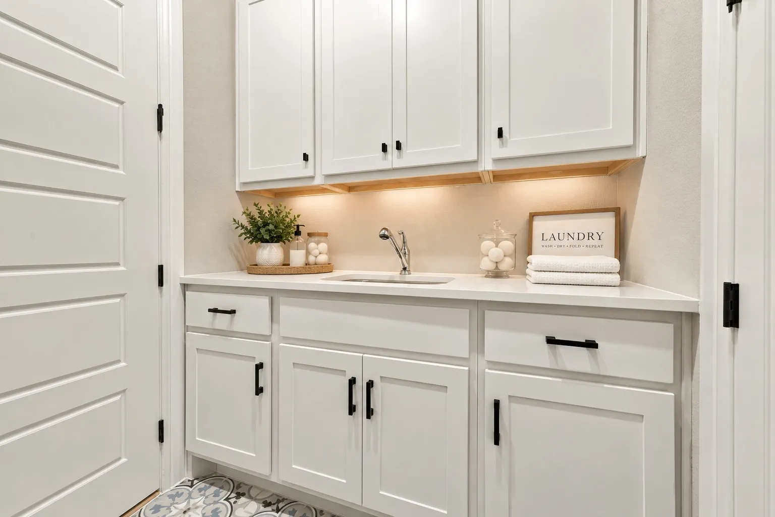 White cabinetry with black hardware, white countertop, undermount sink, and patterned floor tile