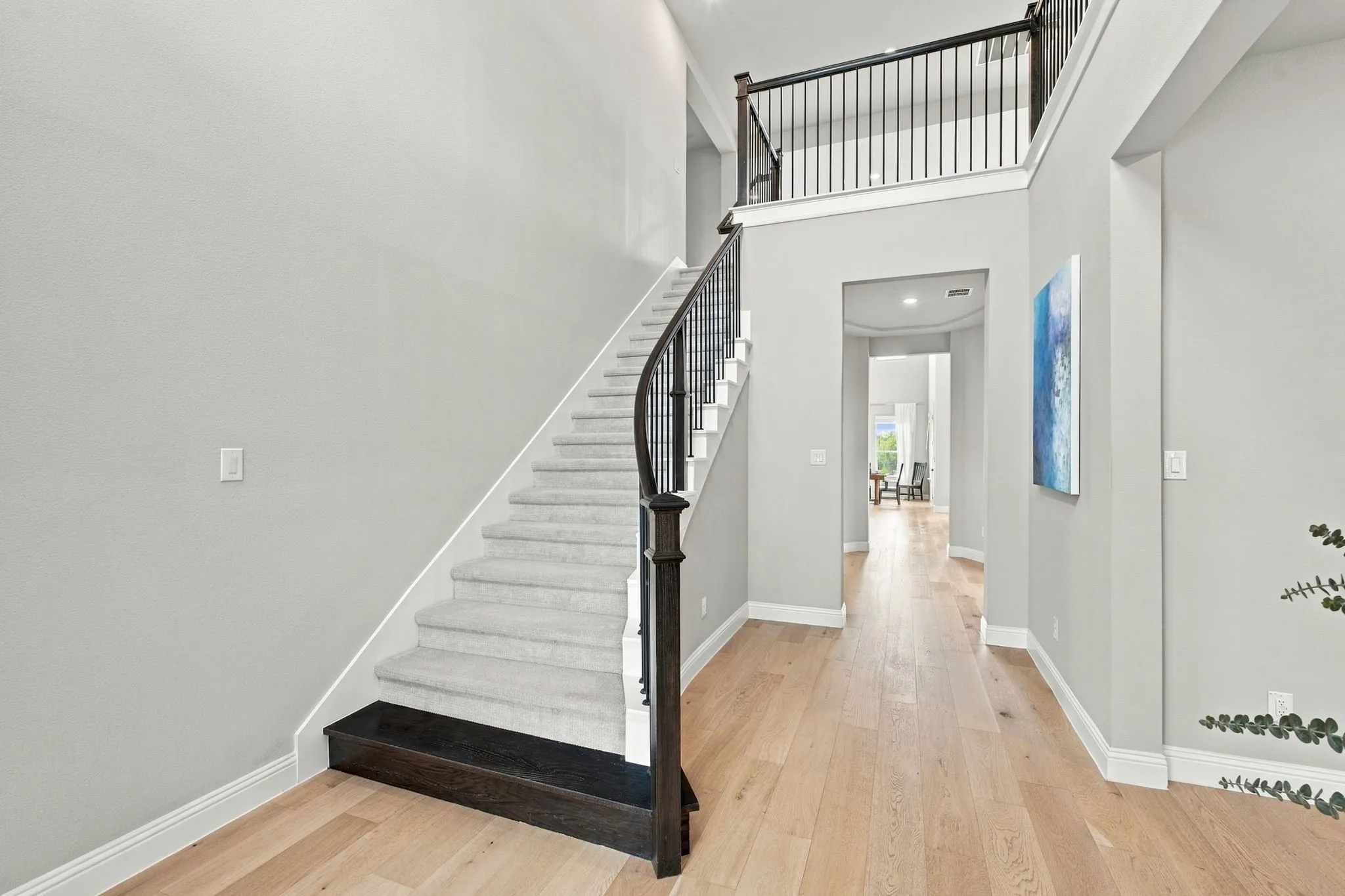 Light wood-finish flooring, two-story ceiling, curved staircase with dark wood-finish banister, carpeted treads, and an upper-level railing