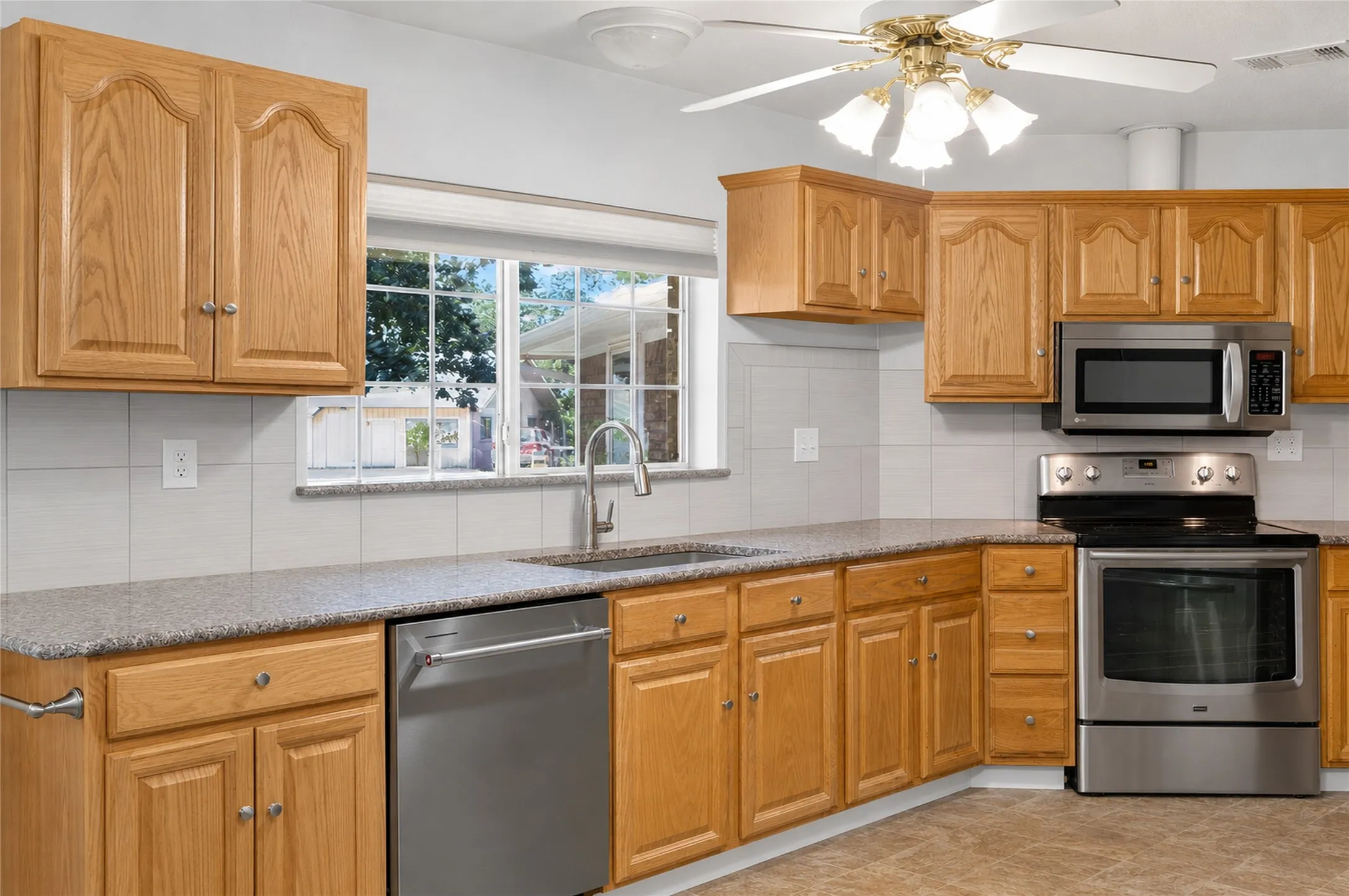 Kitchen featuring wood cabinetry, stainless steel appliances, speckled countertops, and a tile backsplash - Virtually Cleared