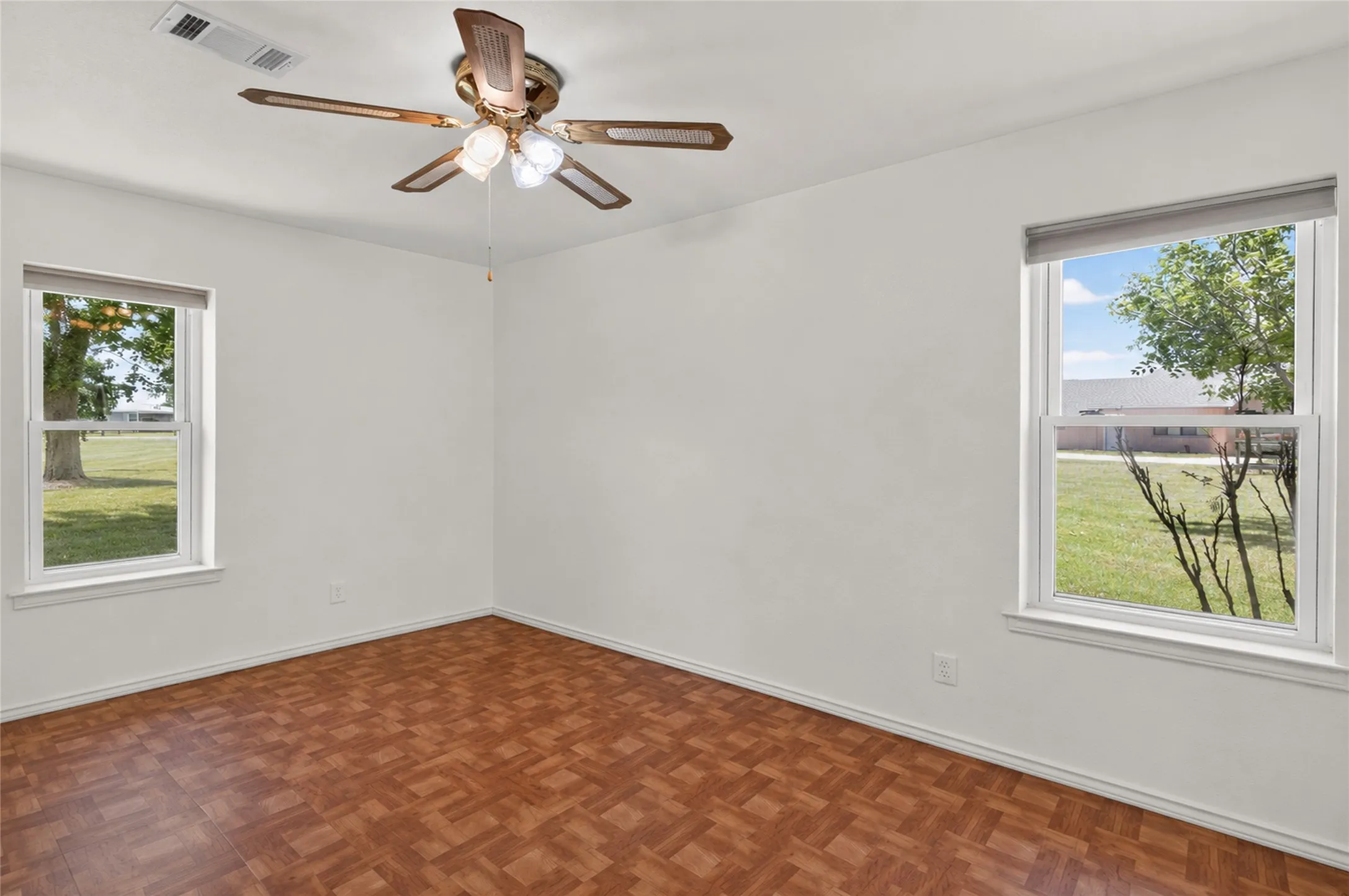 Bright room featuring two windows, wood-finish parquet flooring, and a ceiling fan with integrated lighting - Virtually Cleared