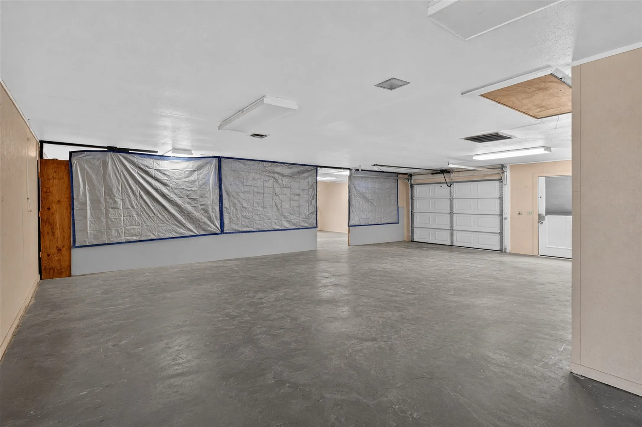 Spacious garage with concrete flooring, fluorescent lighting, and multiple access doors - Virtually Cleared