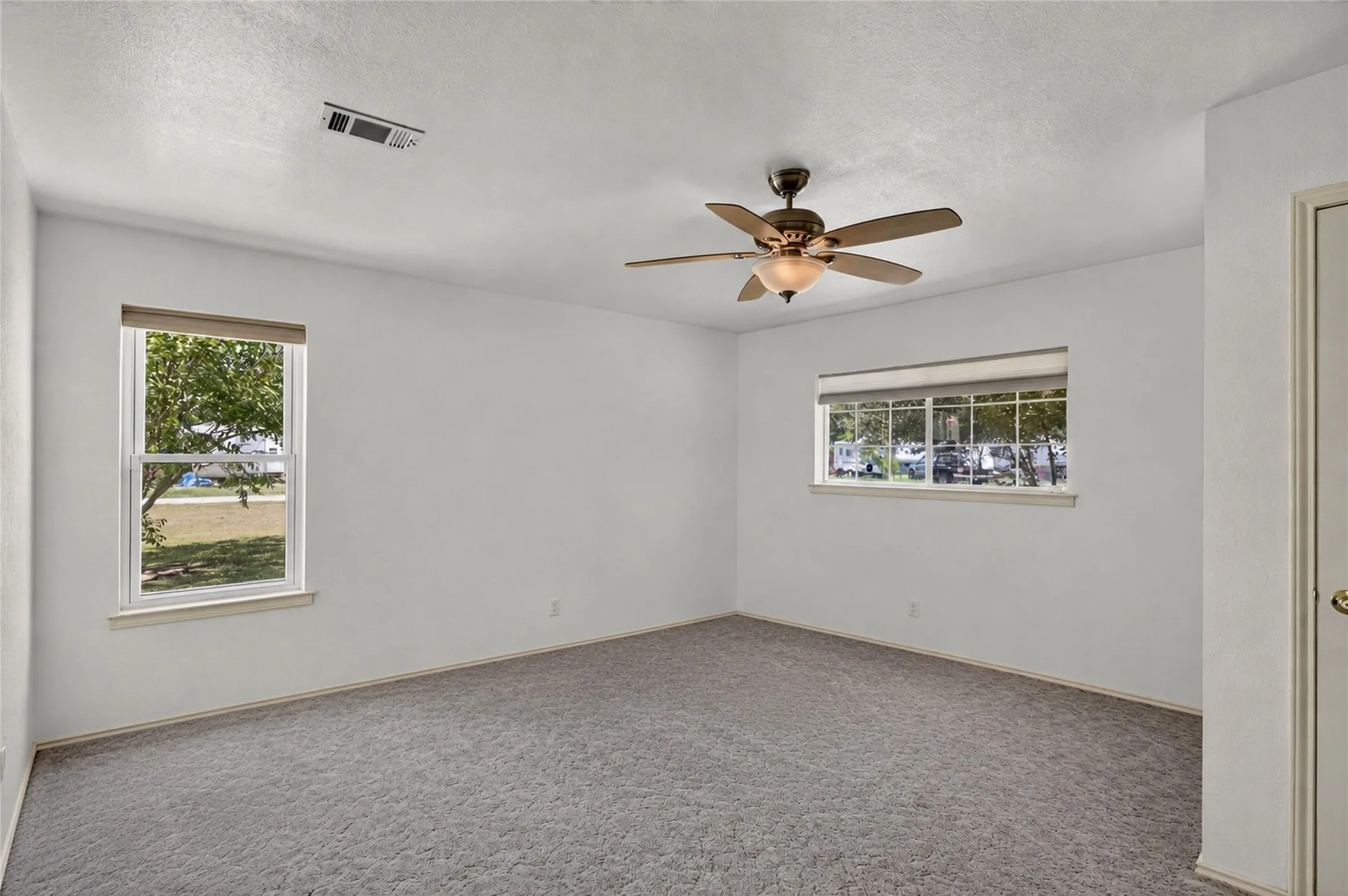 Recessed lighting, ceiling fan with light fixture, gray carpet, two windows with blinds, and white interior door - Virtually Cleared
