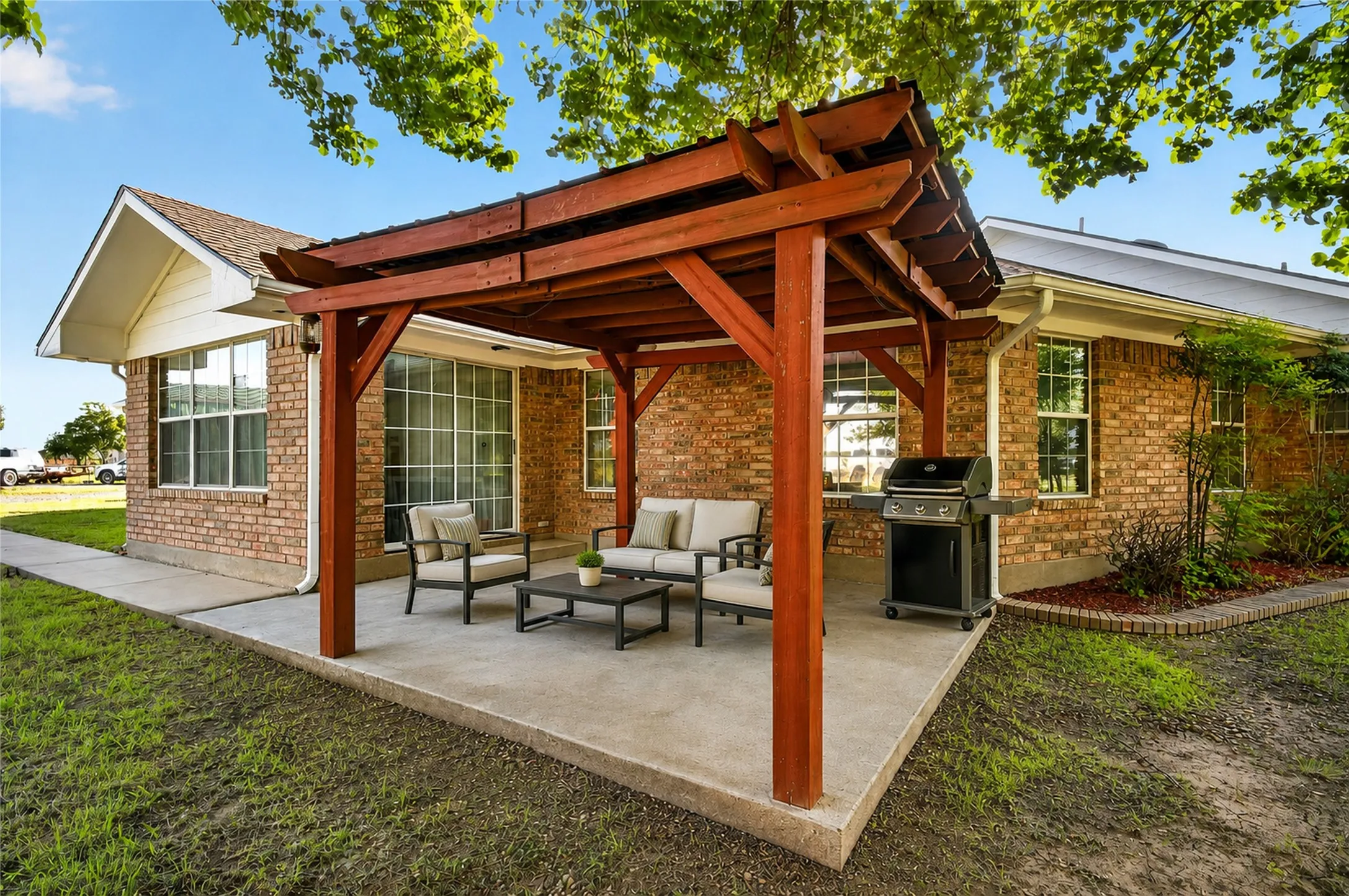 Concrete patio with a wood pergola, brick exterior, and a manicured lawn - Virtually Staged