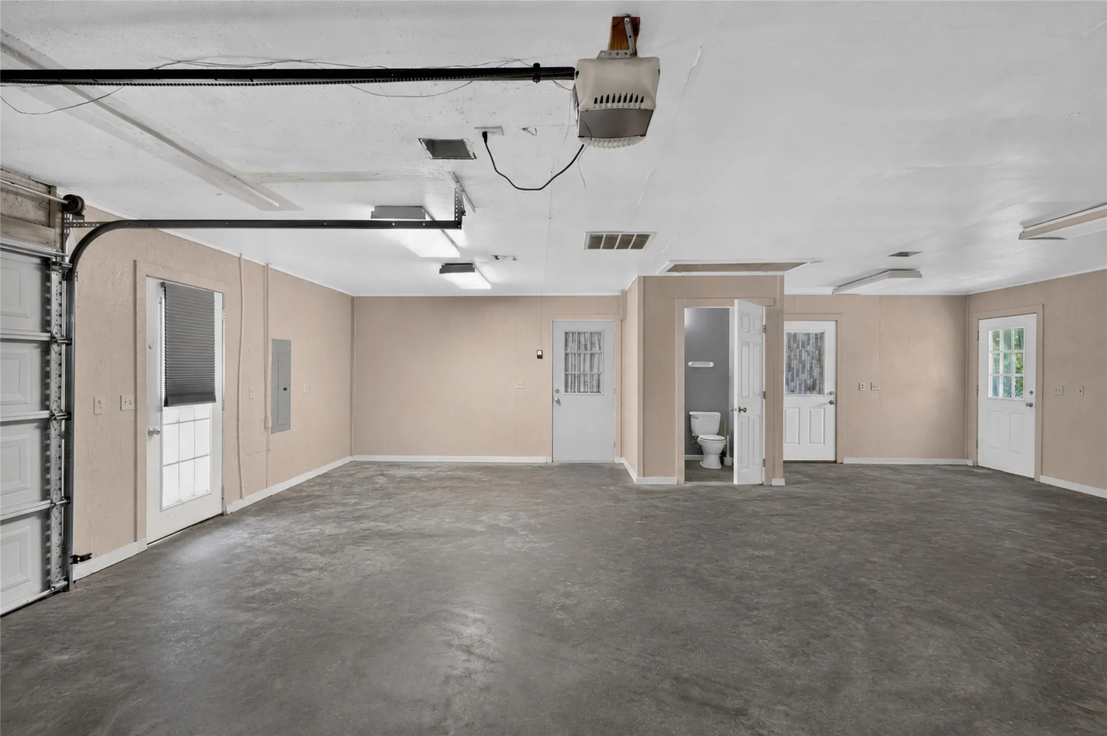 Spacious garage area featuring a concrete floor, multiple entry doors, and overhead lighting - Virtually Cleared