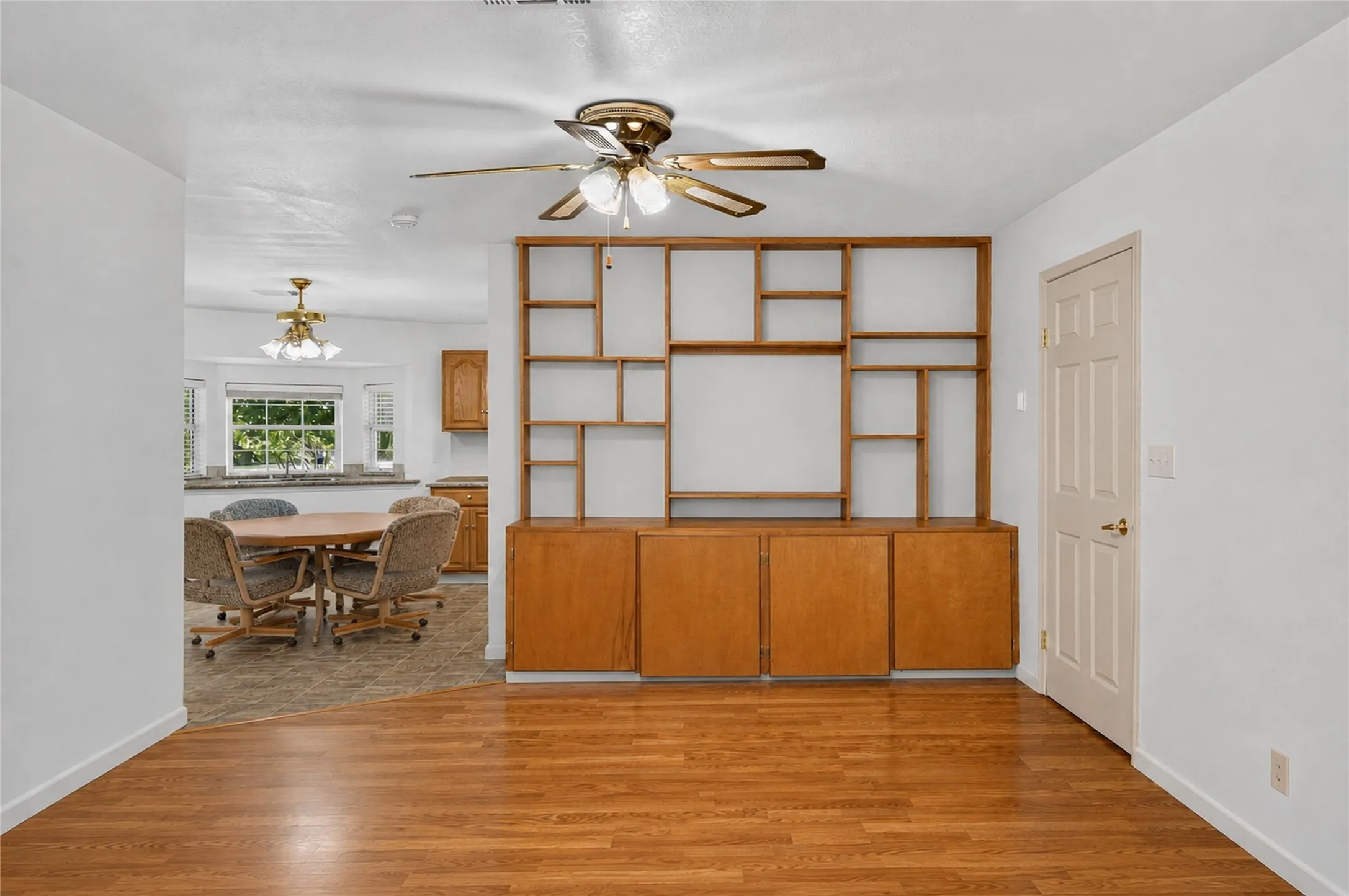 Hardwood-style flooring throughout, built-in shelving with lower cabinetry, and a ceiling fan with integrated lighting - Virtually Cleared