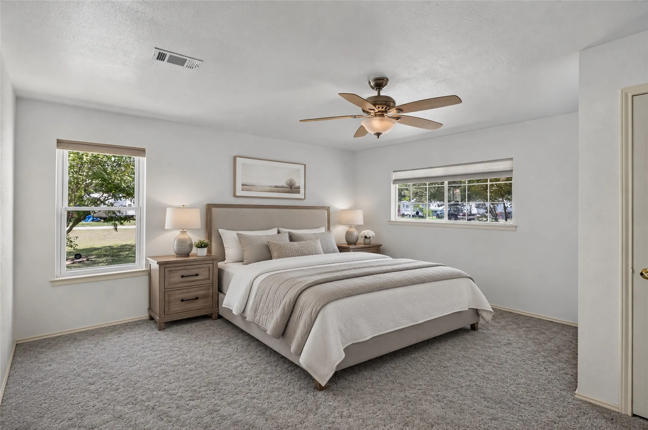 Carpeted flooring, white painted walls, two windows with blinds, and a ceiling fan with integrated lighting - Virtually Staged